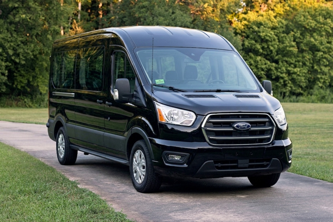 Black Ford Transit van parked on a paved driveway with green grass and trees in the background.
