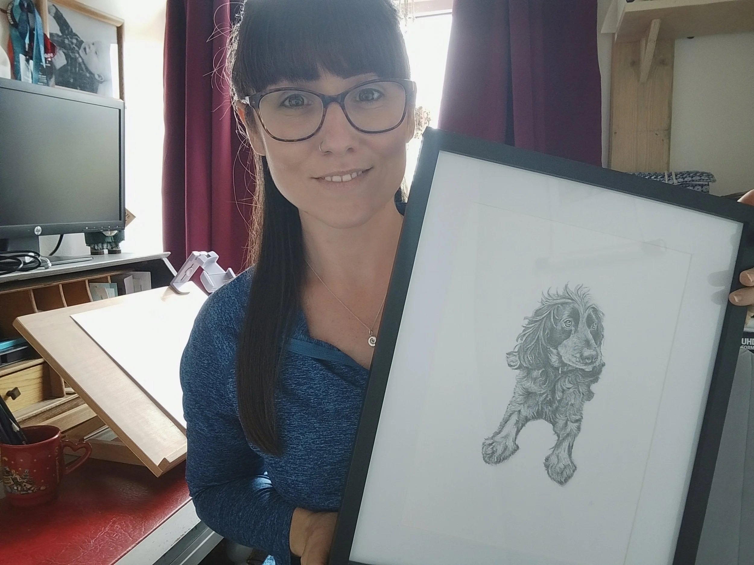 A woman with long dark hair, glasses, and a nose piercing holding a framed artwork of a lion.