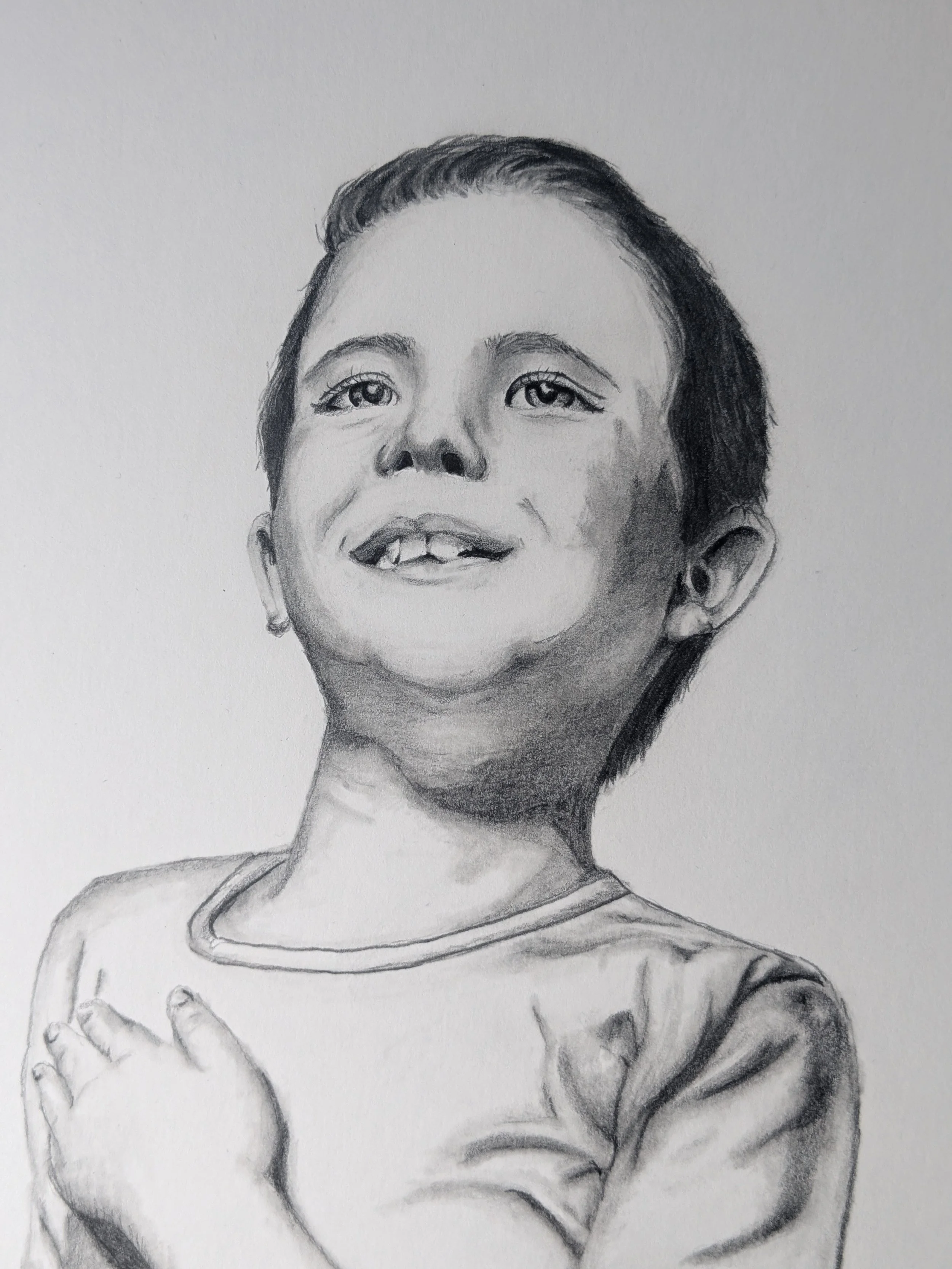 A realistic pencil sketch of a young boy with a cheerful smile, short hair, wearing a t-shirt, with his hand resting near his chin.