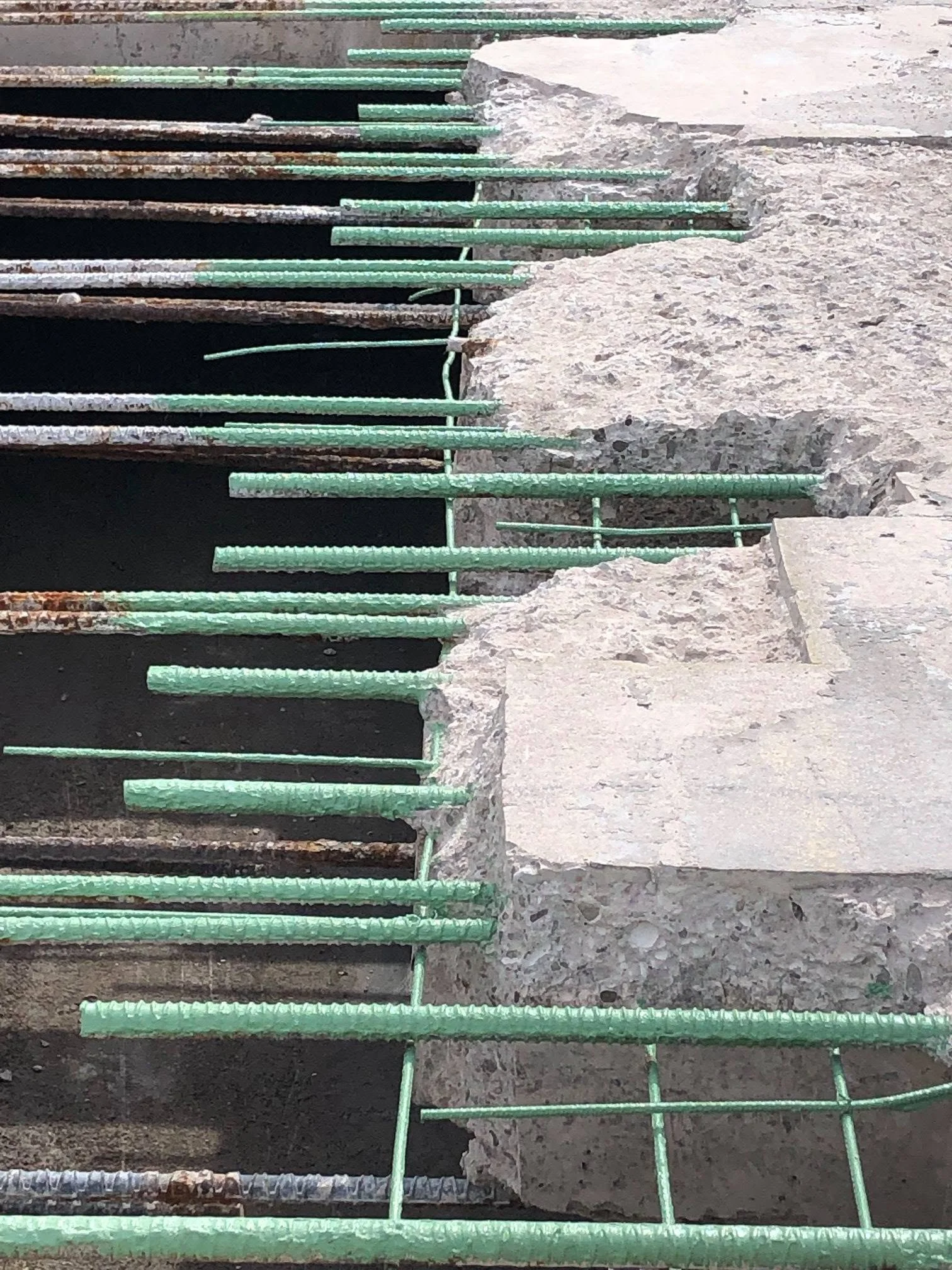 Close-up of a construction site showing a section of concrete with rebar and green metal supports used for reinforcement.