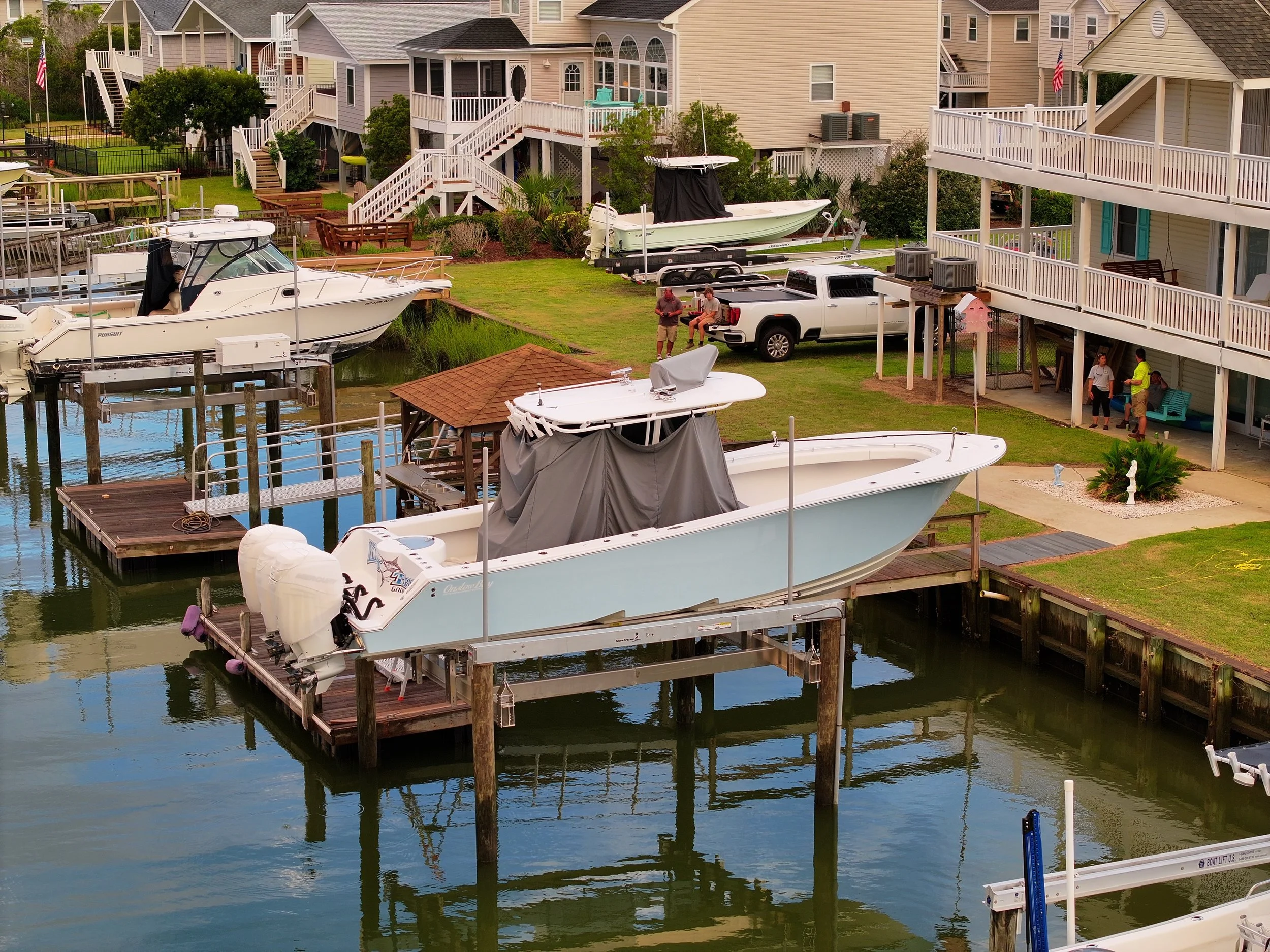 View of a waterfront backyard with boats, a white truck, and multi-story houses with decks.