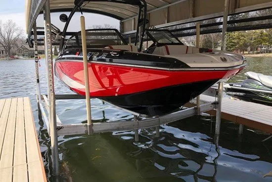 A red and white speedboat stored on a boat lift above the water at a dock.