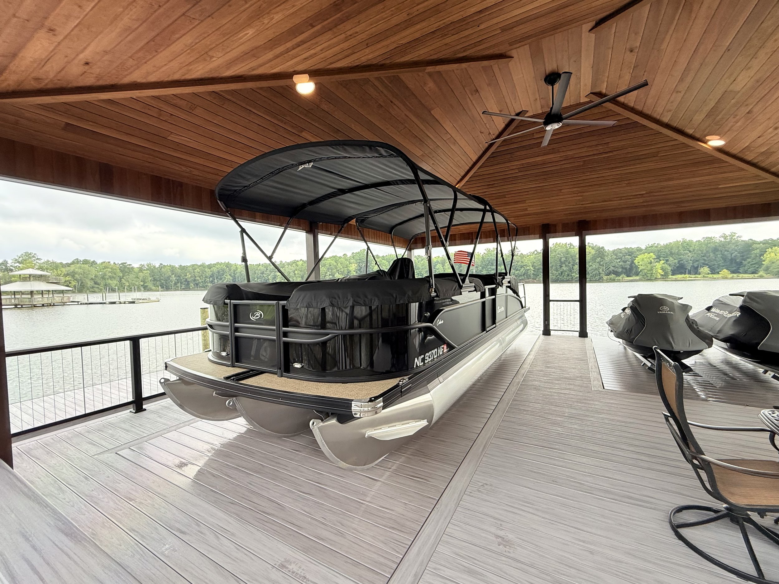 Covered patio overlooking a lake with a pontoon boat, boat motors, and a dock in the background.