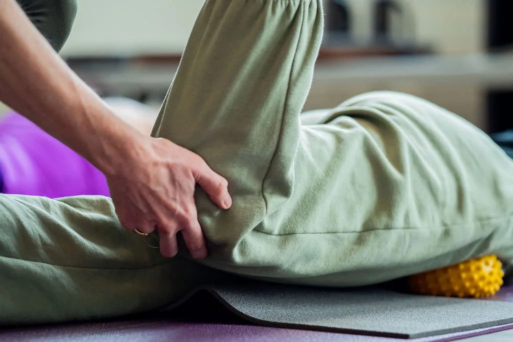 Person performing a massage or physical therapy on someone lying face down on a mat, using a yellow foam roller.