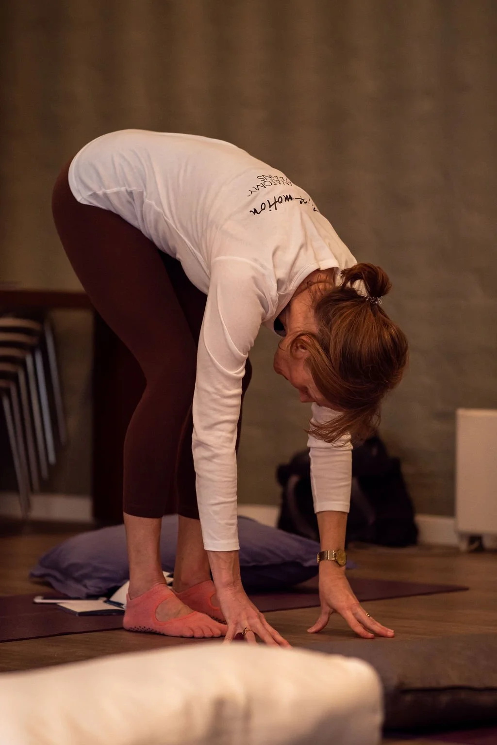A woman practicing yoga in a bent-over forward fold position on a yoga mat indoors.