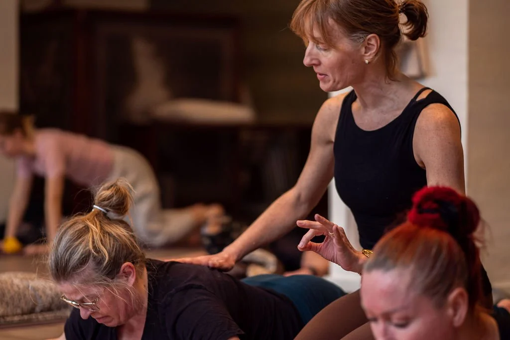 Instructor guiding a yoga class with multiple women practicing yoga in a studio.