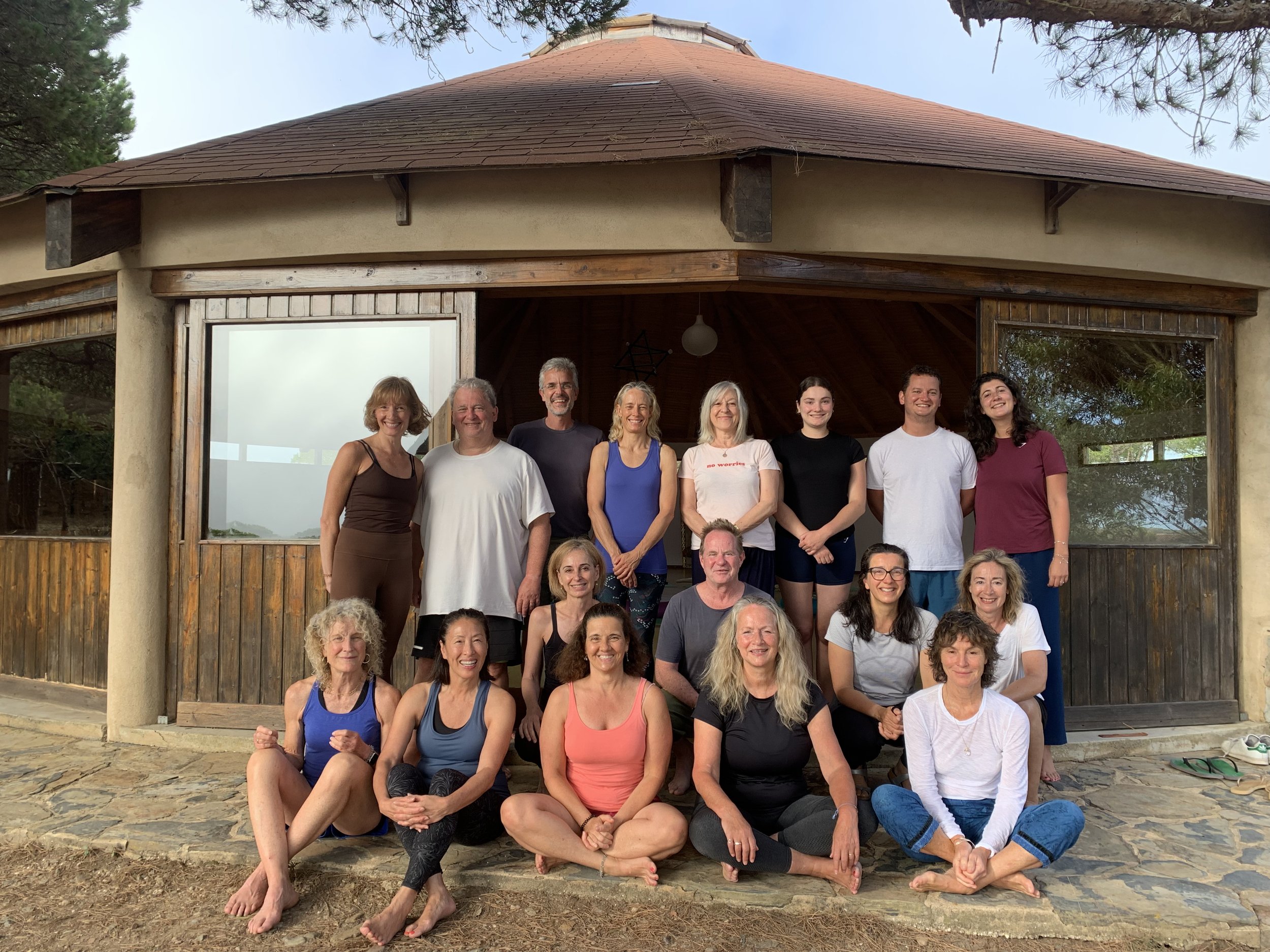 Group of people in athletic clothing gathered outside a wooden building, some sitting and some standing, smiling for a photo.