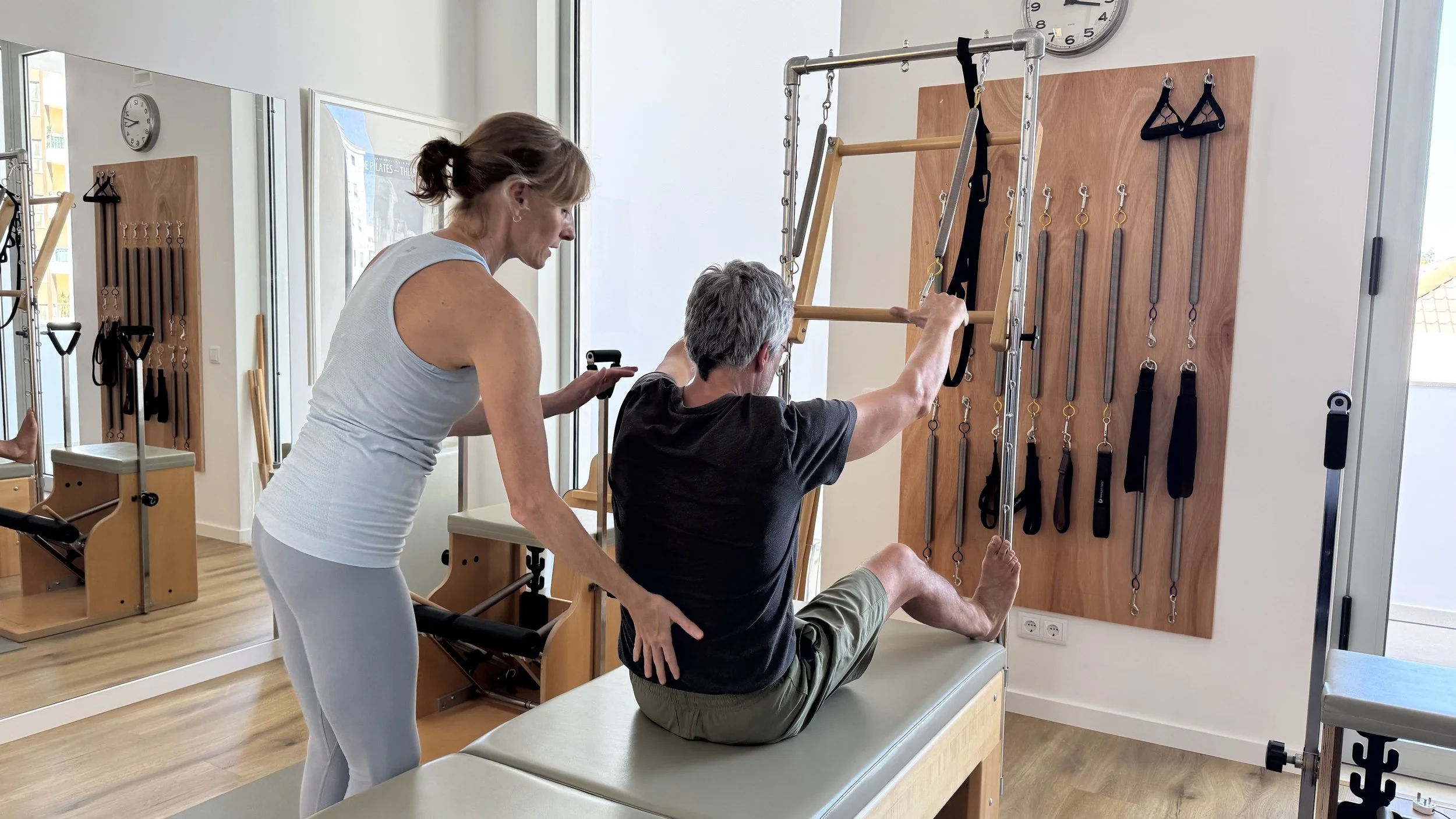 A woman assisting a man with a seated rehabilitation exercise in a physical therapy clinic, focusing on shoulder movement.
