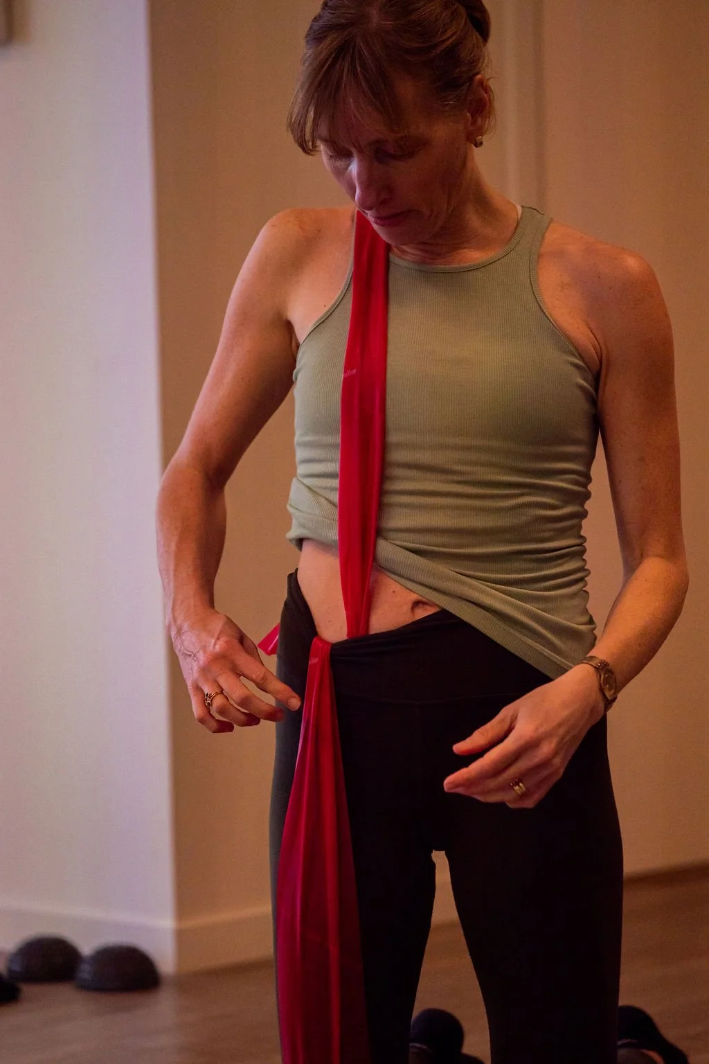 A woman adjusting a red cloth tied around her waist in a room with dumbbells on the floor.