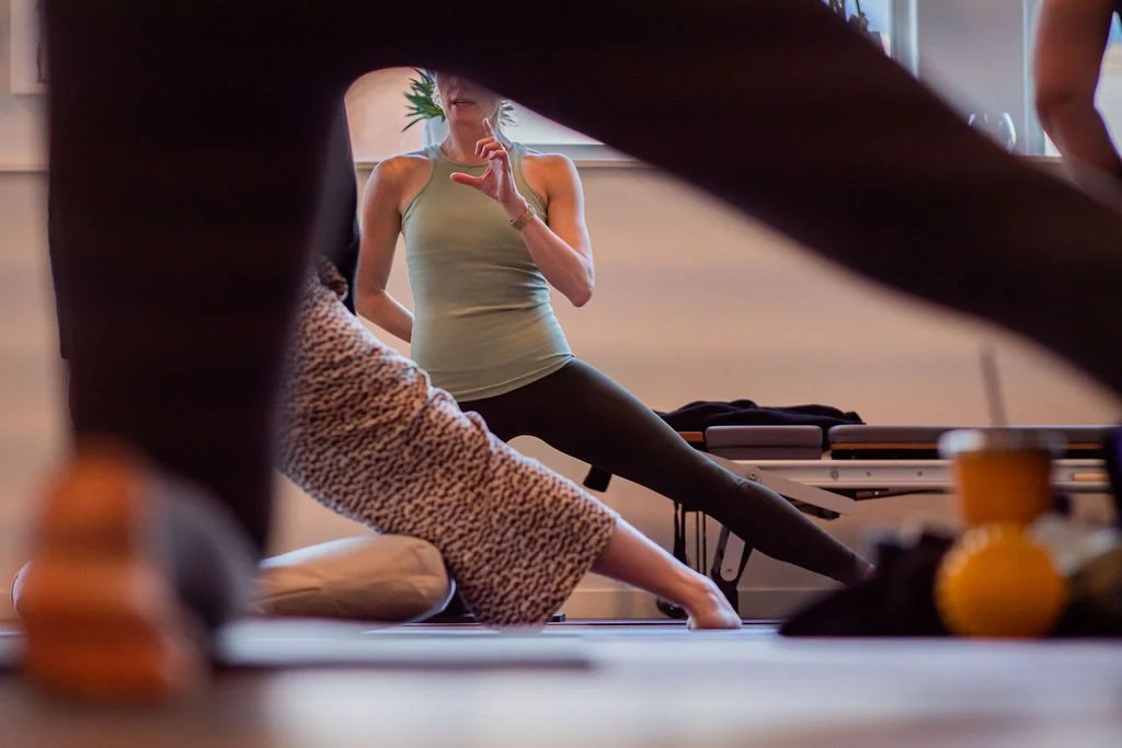 Someone practicing yoga with an instructor in a yoga studio, with their legs and arms in various positions, and the instructor guiding a stretch.