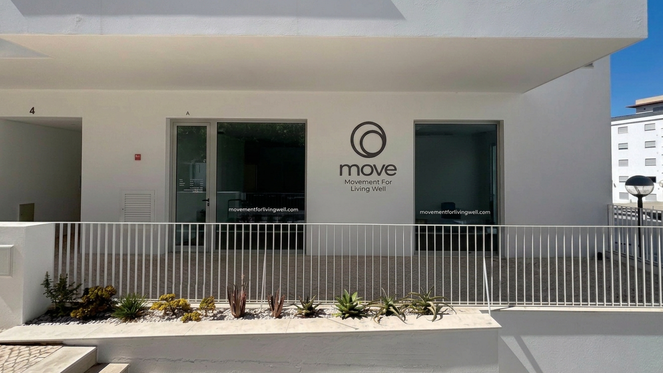 Front view of a modern white building with a balcony, featuring a logo and sign that reads 'move, Movement For Living Well', and a small garden with succulents in front.