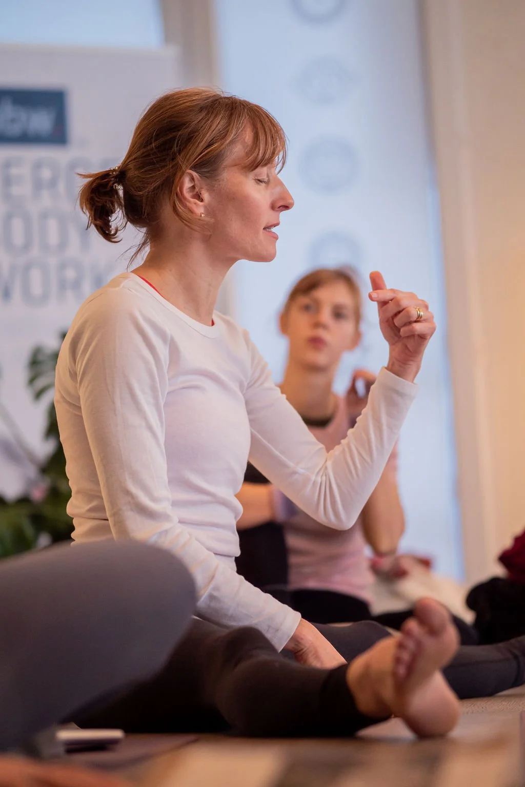 Woman practicing yoga at a meditation class, seated cross-legged with eyes closed and in a peaceful pose.