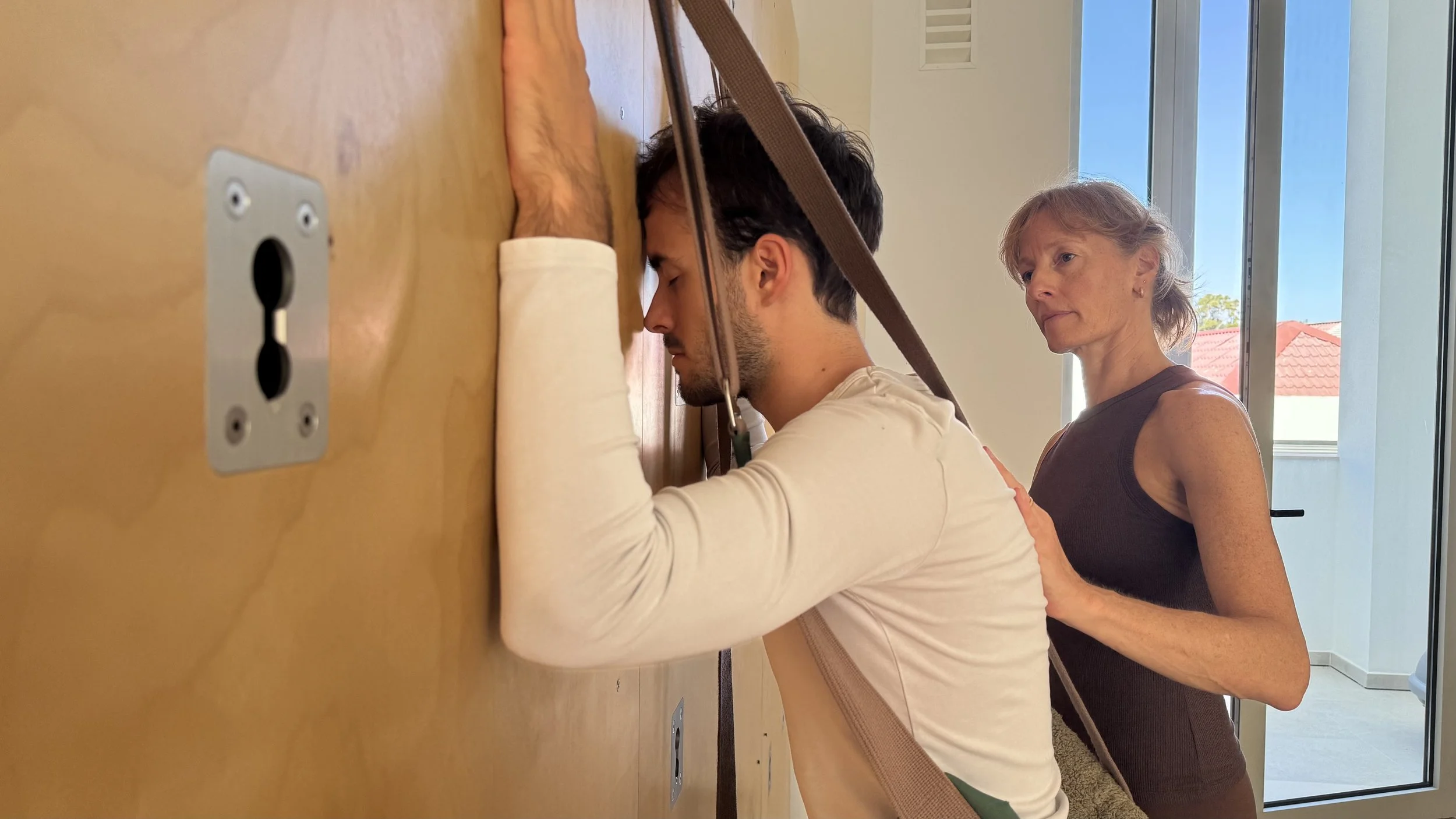Stephanie assisting a student doing yoga in a room with large Yoga Wall.