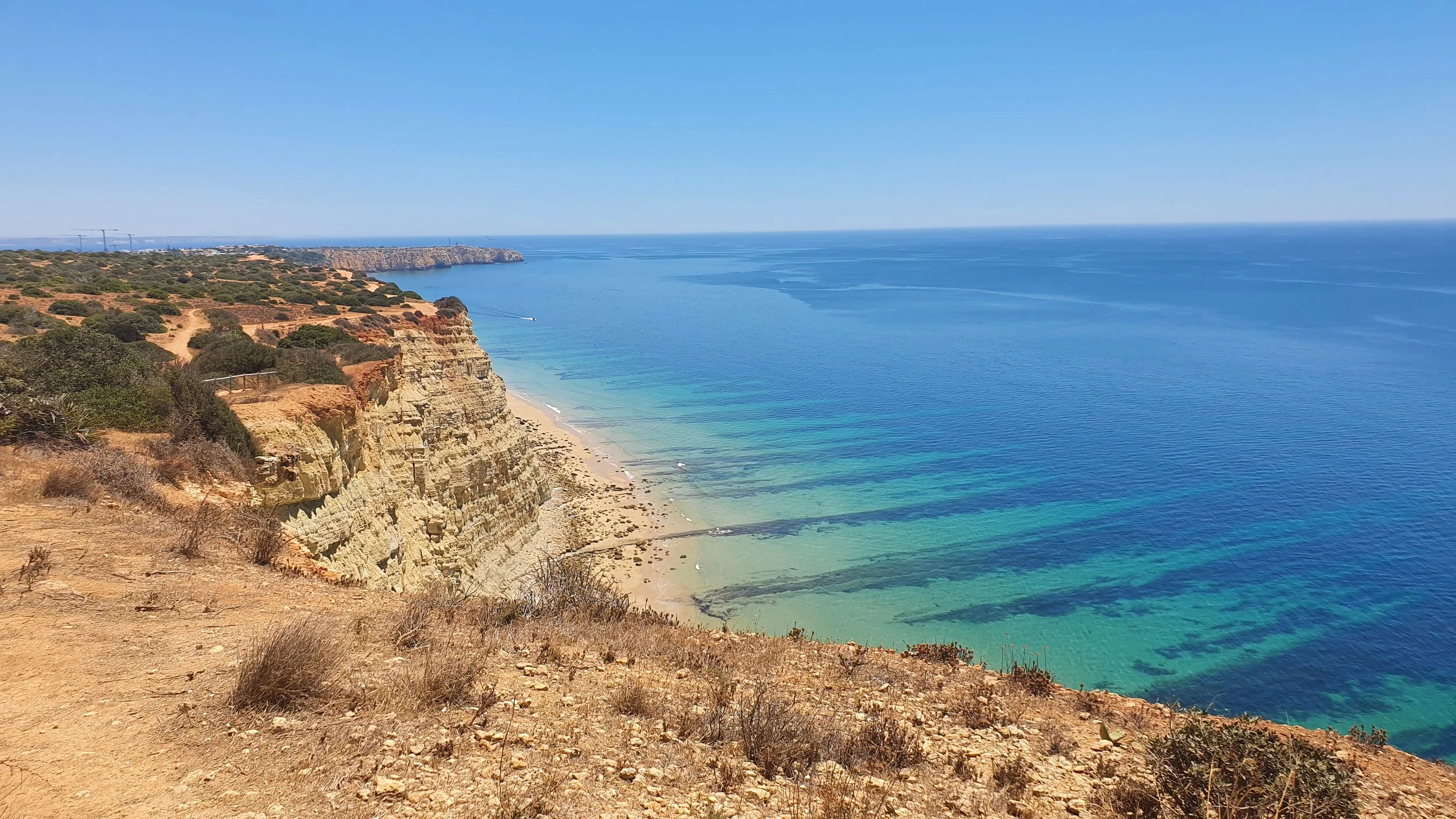 Cliffs overlooking a sandy beach and clear blue ocean under a bright sky.