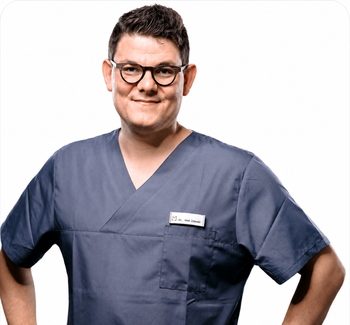 Ein männlicher Arzt trägt eine dunkelblaue medizinische Uniform und eine Brille, lächelt freundlich, vor weißem Hintergrund.