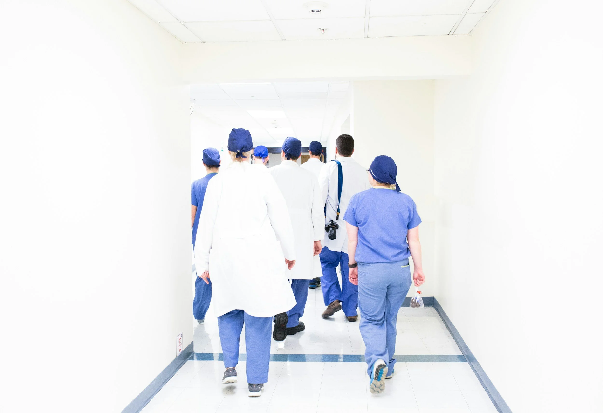 Group of medical professionals walking down hospital corridor, wearing scrubs and caps.