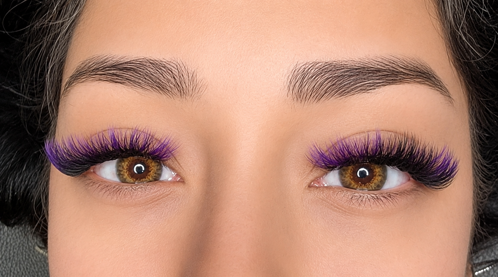 Close-up of a person's eyes with long purple eyelashes and brown irises.