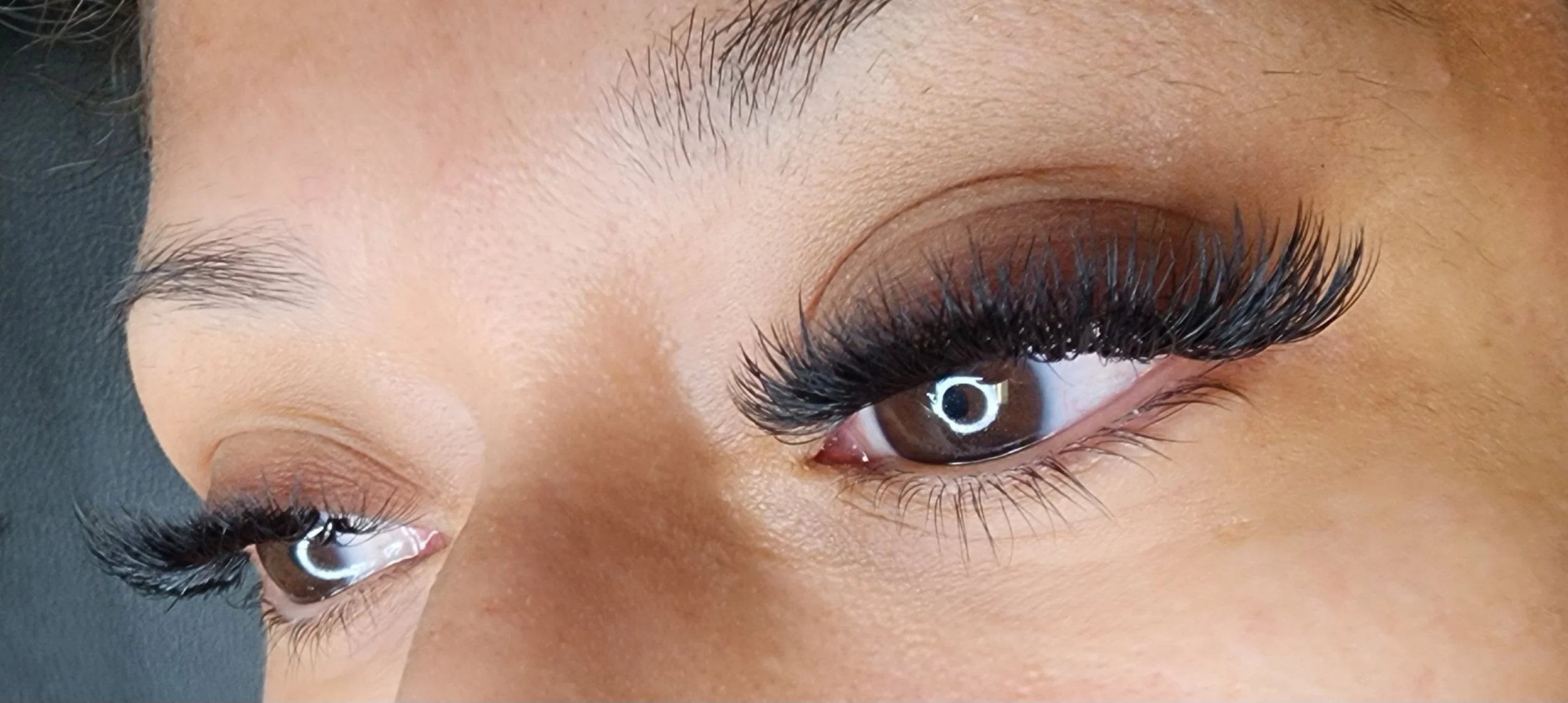 Close-up of a person's eye with long, curled false eyelashes, brown eye color, and well-groomed eyebrows.
