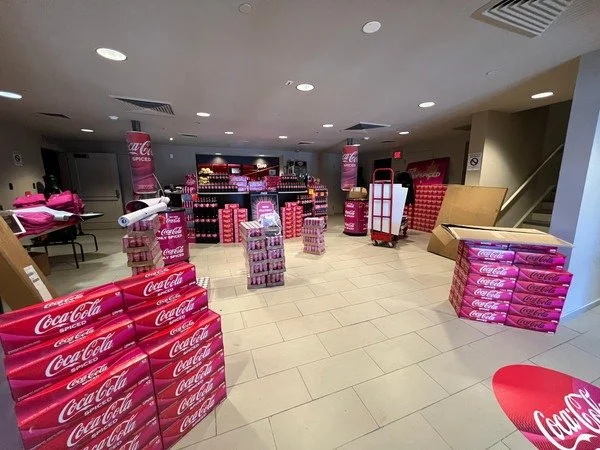 Indoor space with Coca-Cola pink packaging and displays, possibly in preparation for an event or promotion.