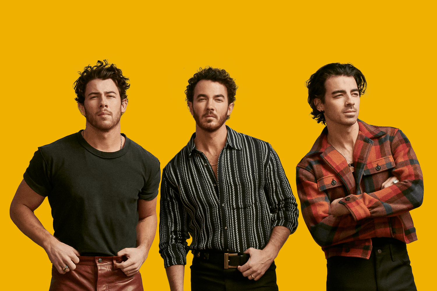 Three young men with dark, wavy hair and light skin standing against a yellow background, dressed in casual, stylish clothing.