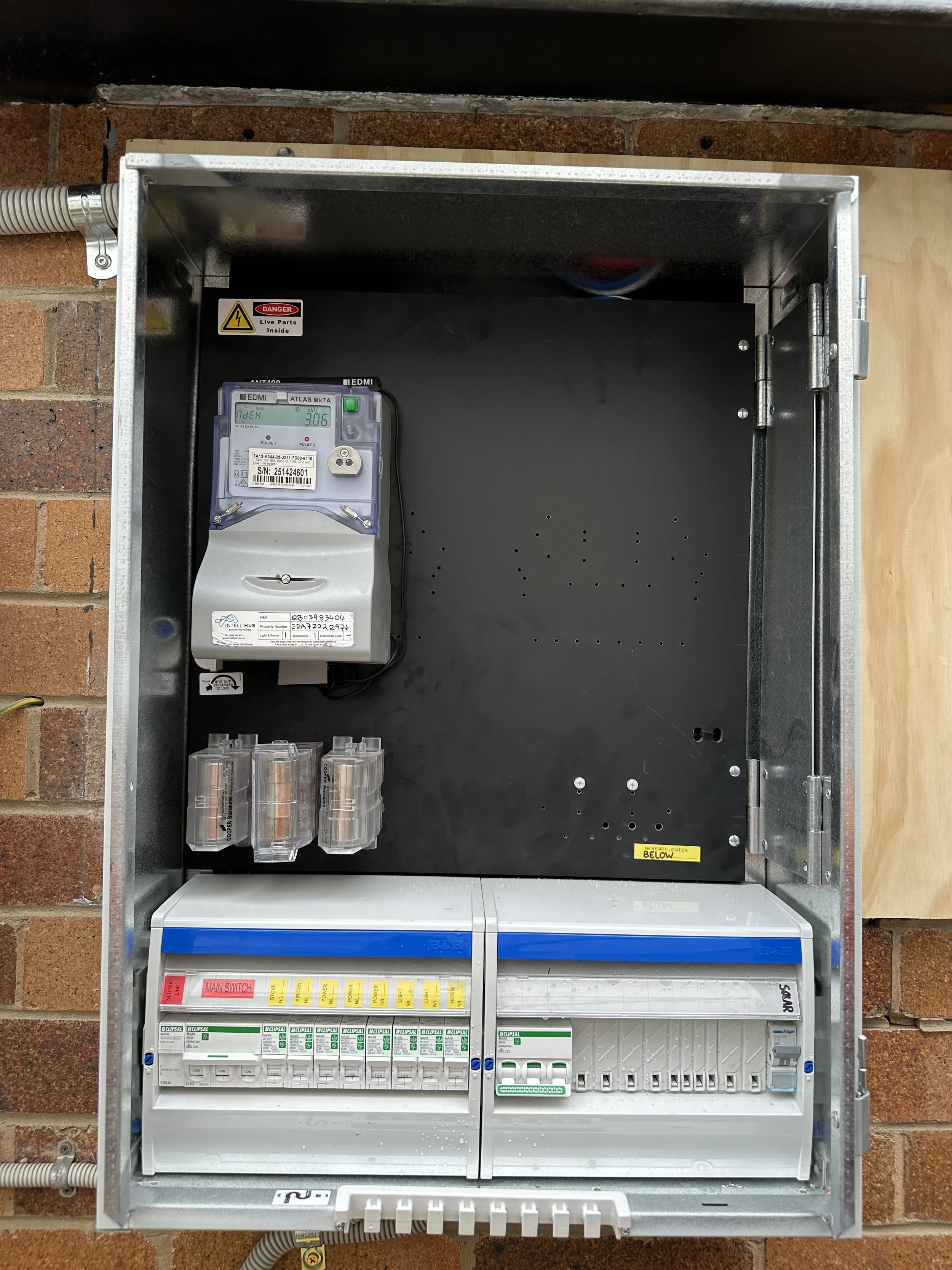 An electrical meter and a circuit breaker panel inside a metal box on a brick wall.