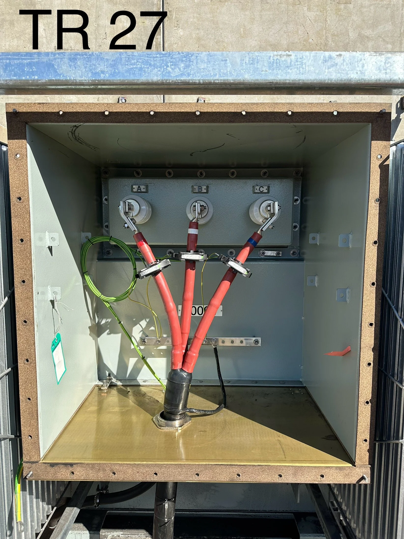 Electrical components inside a metal cabinet, with red and black cables connected to three labeled fuse holders 'A,' 'B,' and 'C,' and some green wires, mounted on a faux wood base.