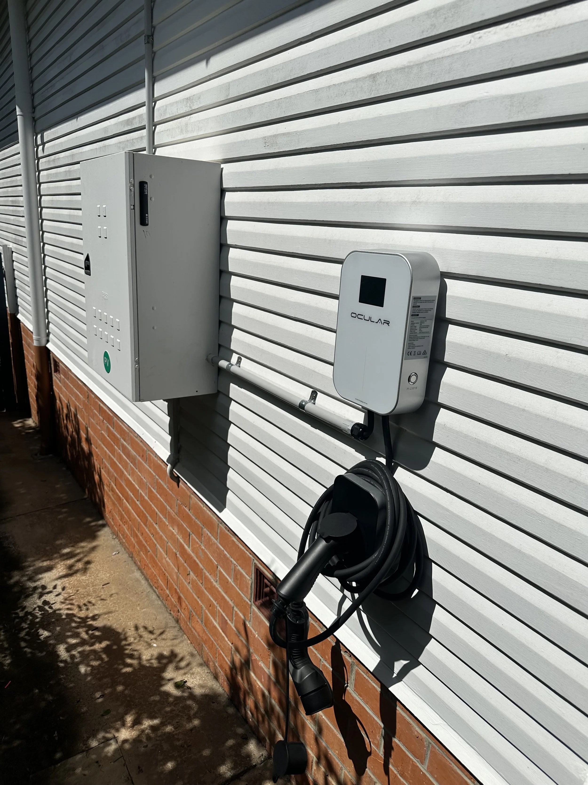 Outside view of a white house wall with an electric vehicle charging station and a charging cable hanging down.