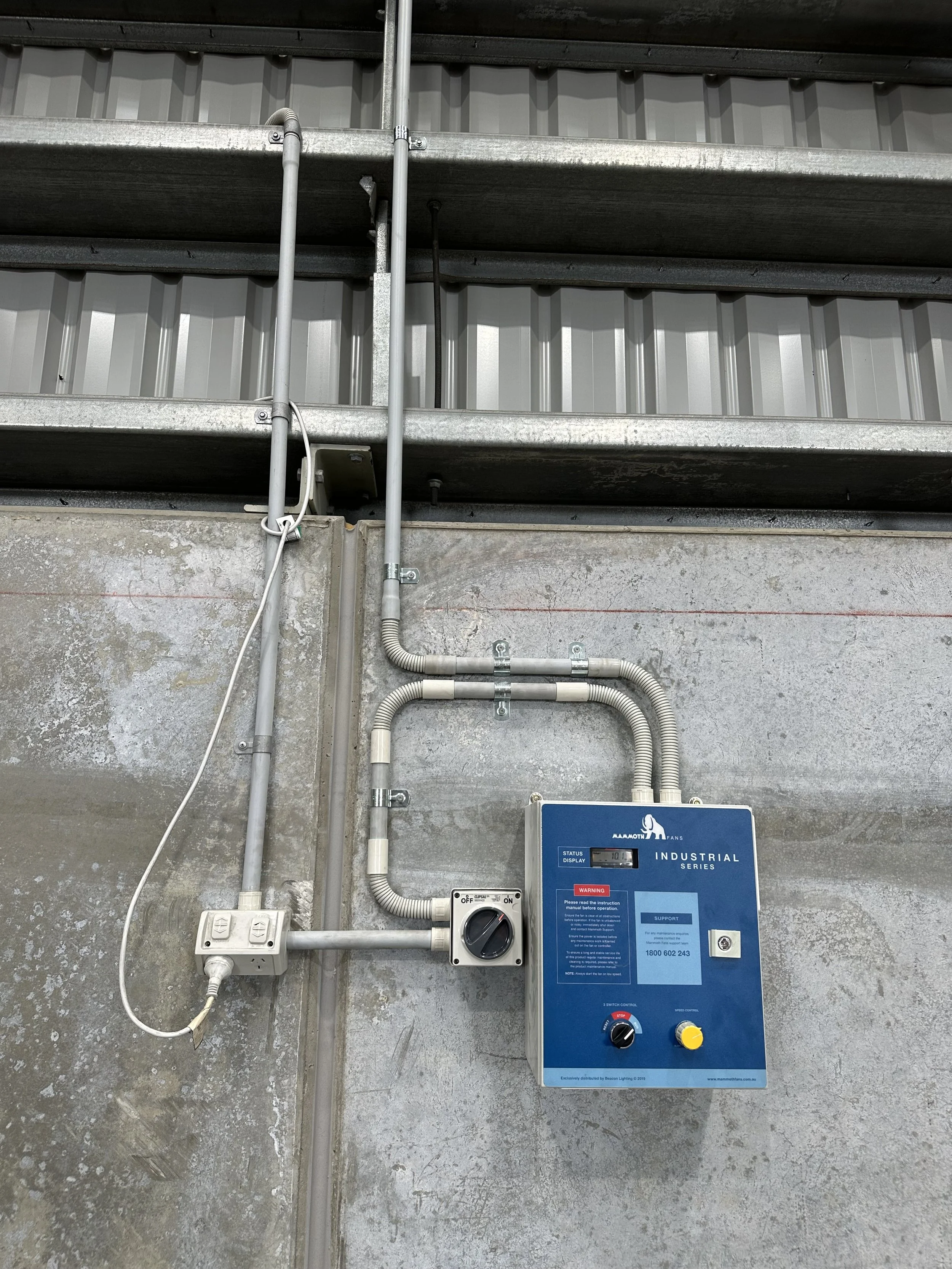 Industrial electrical control box with various cables and conduit pipes mounted on a concrete wall.