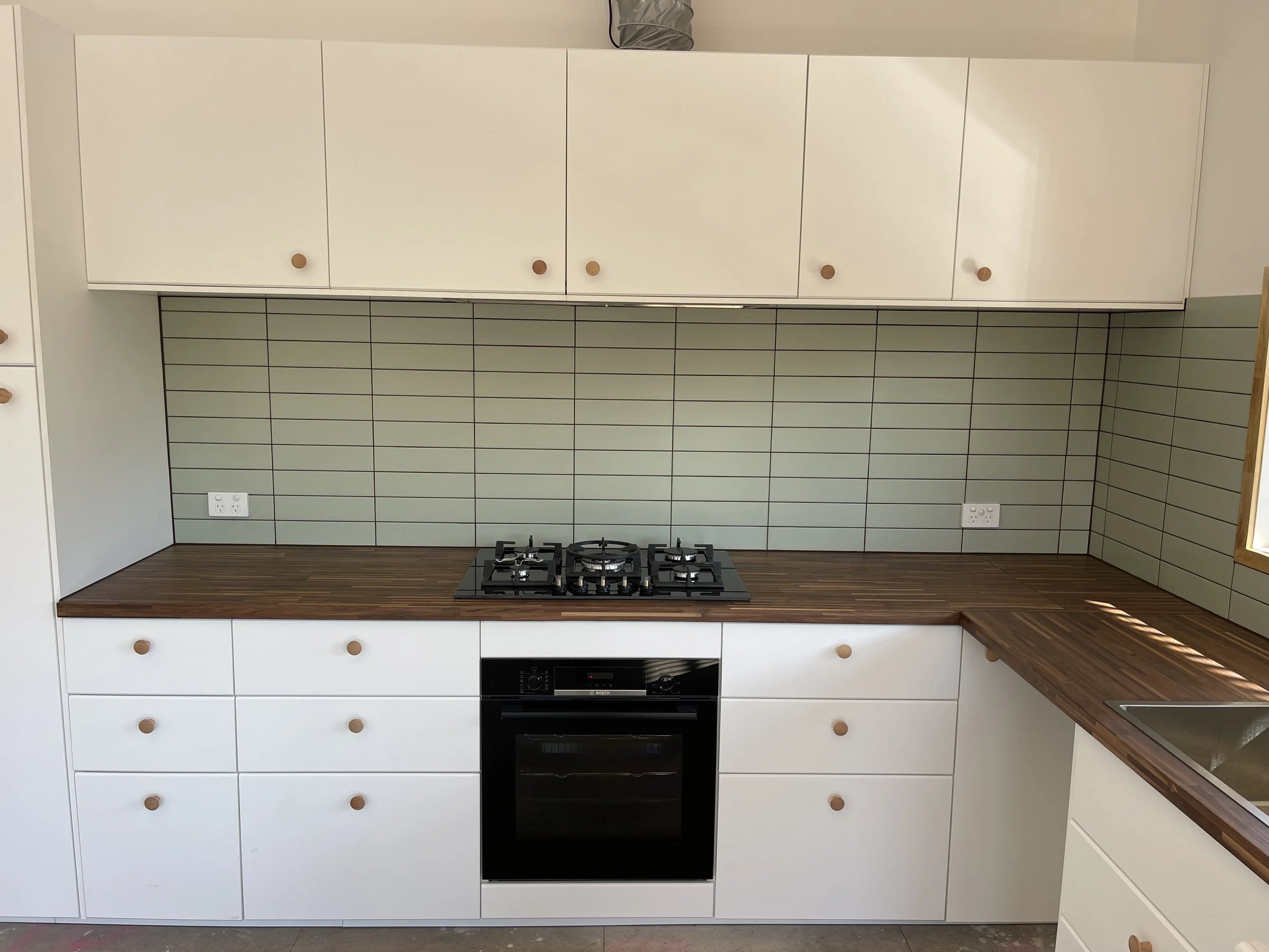 White kitchen cabinets with round wooden knobs, a wooden countertop, a tiled backsplash, a gas stove with four burners, and a built-in oven, with electrical outlets on the wall.