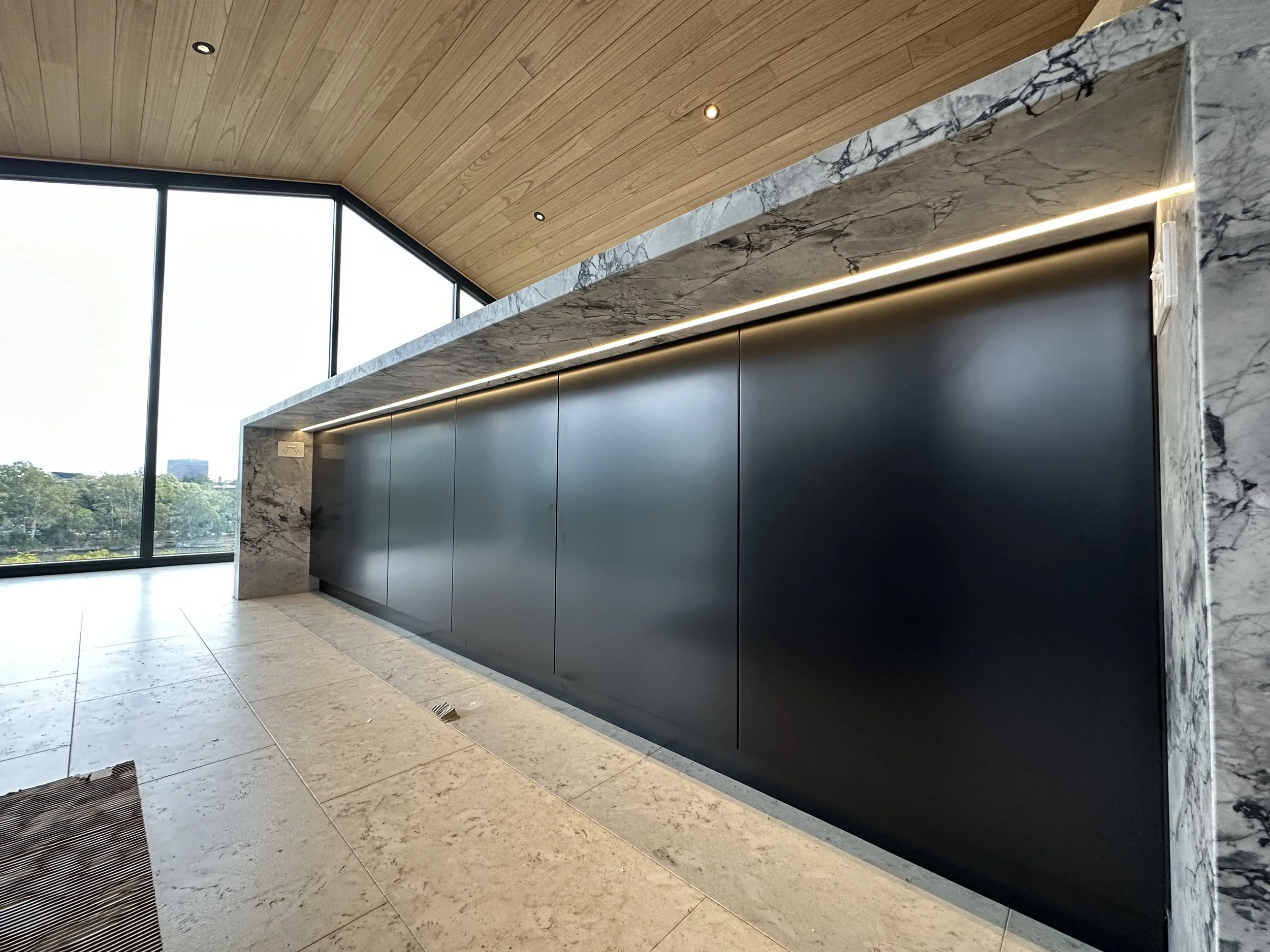 Modern interior with large window, marble and black wall, wooden ceiling, tiled floor, and recessed lighting.