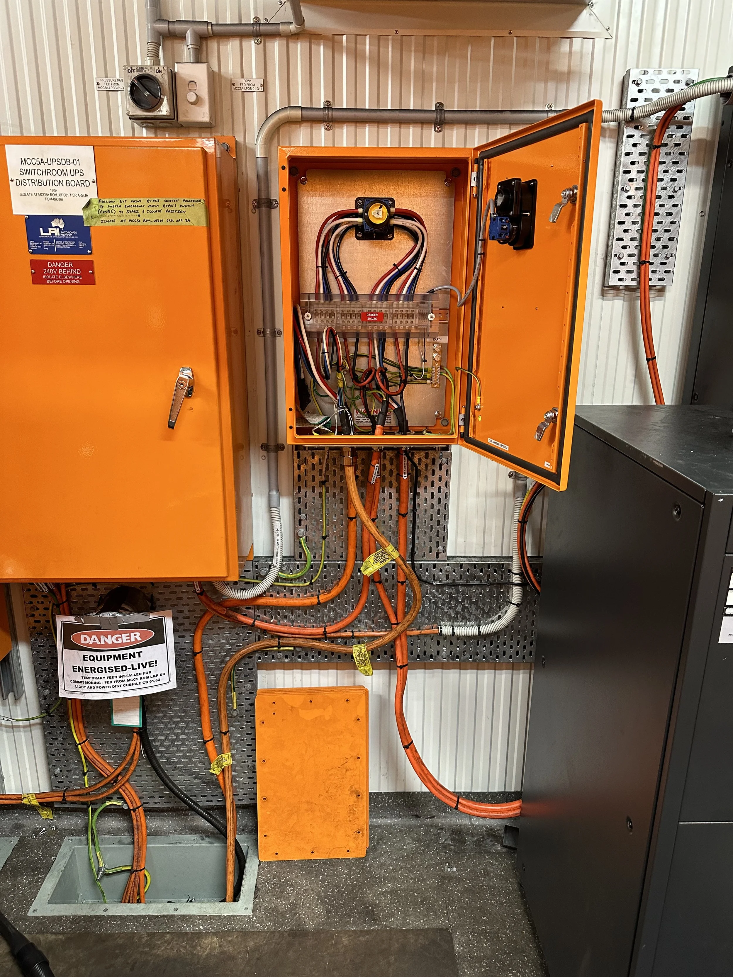 An electrical control panel with orange enclosure, containing various wires, circuit breakers, and labels. There are warning signs indicating danger and equipment energization.