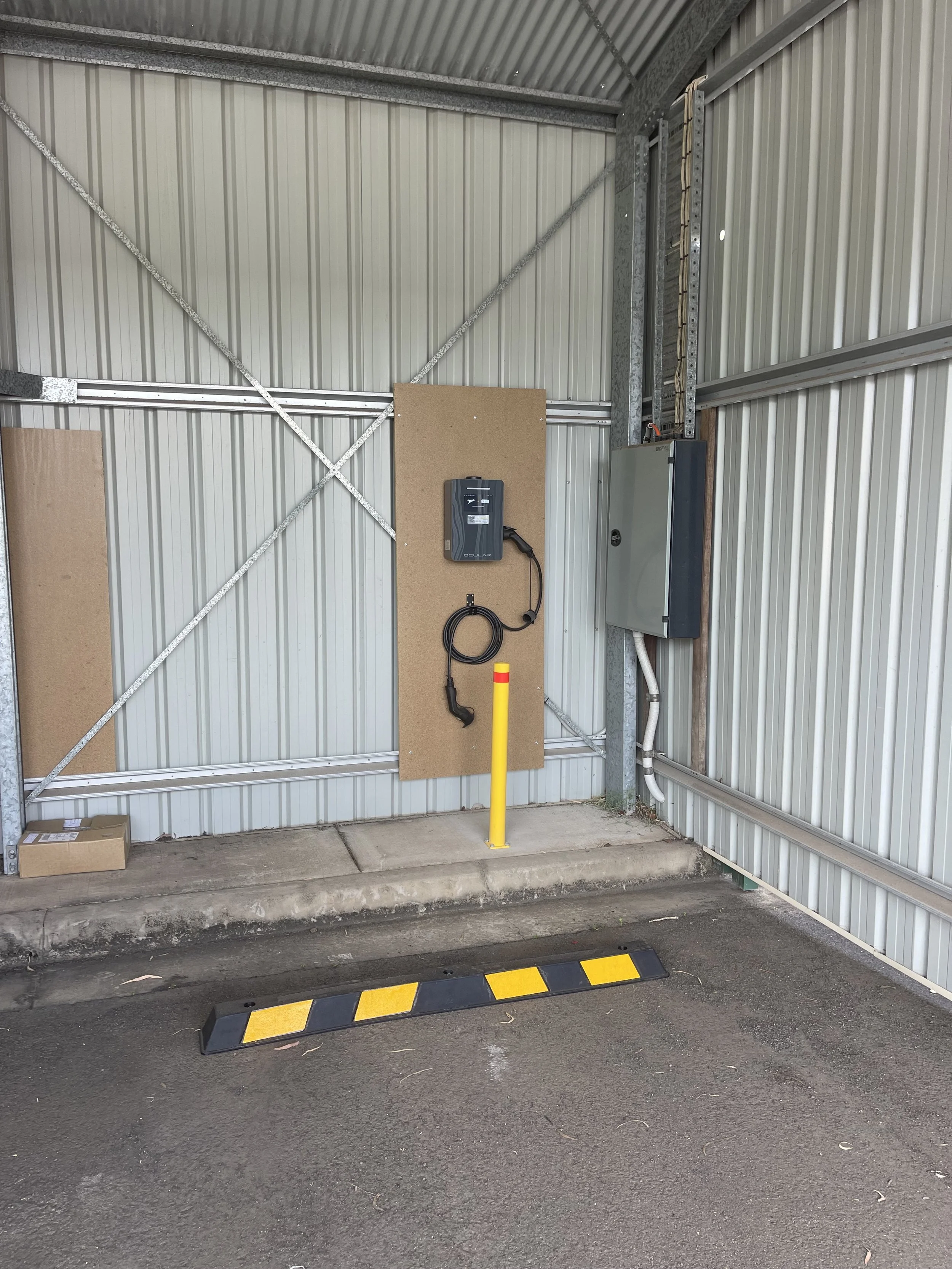 Industrial metal wall and ceiling with electrical and charging equipment, yellow and black parking stop in driveway, painted curb stopper.