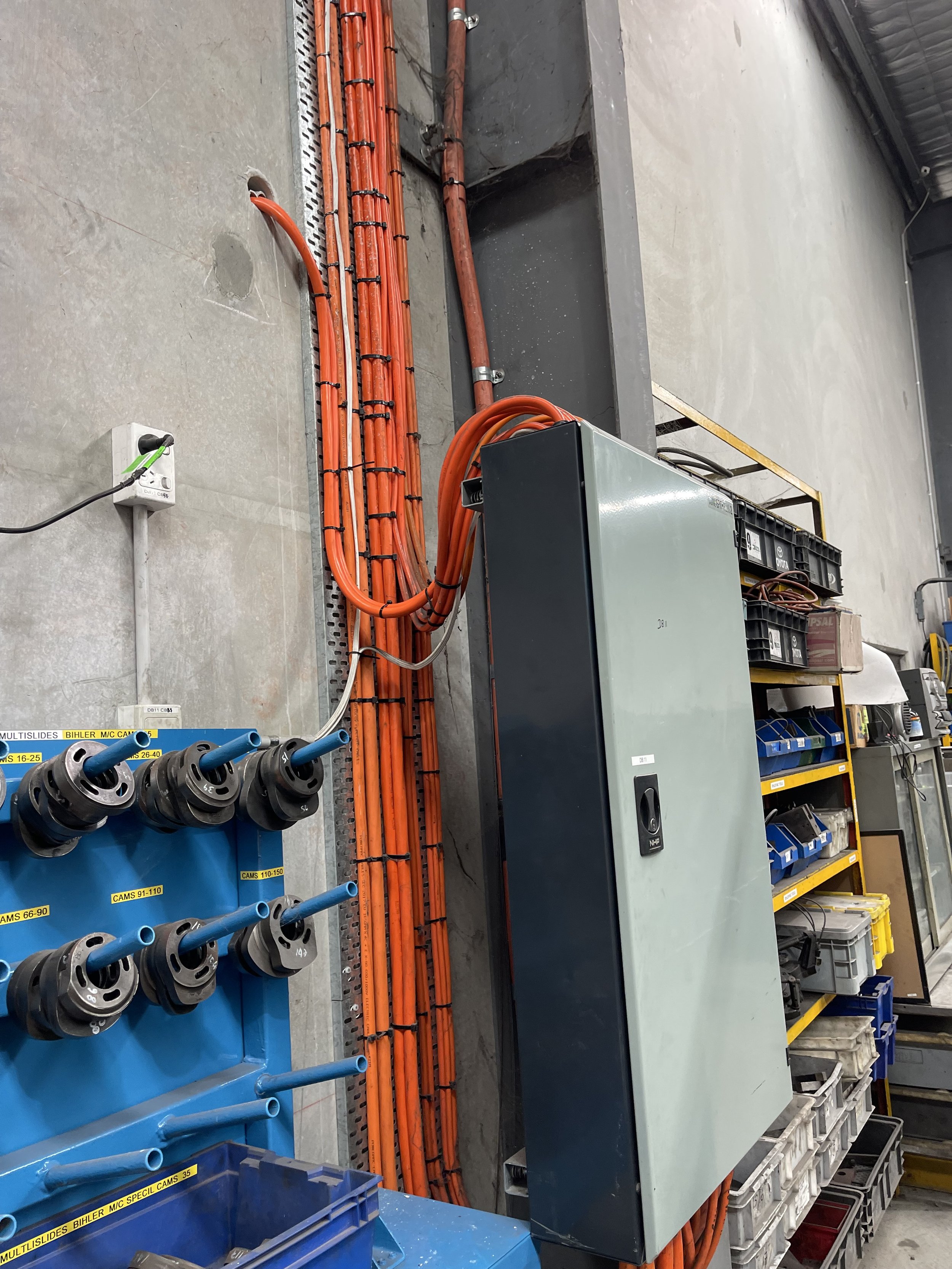 Workshop with organized tools and electrical wiring, including neatly coiled orange cables on a rack and other supplies on shelves.