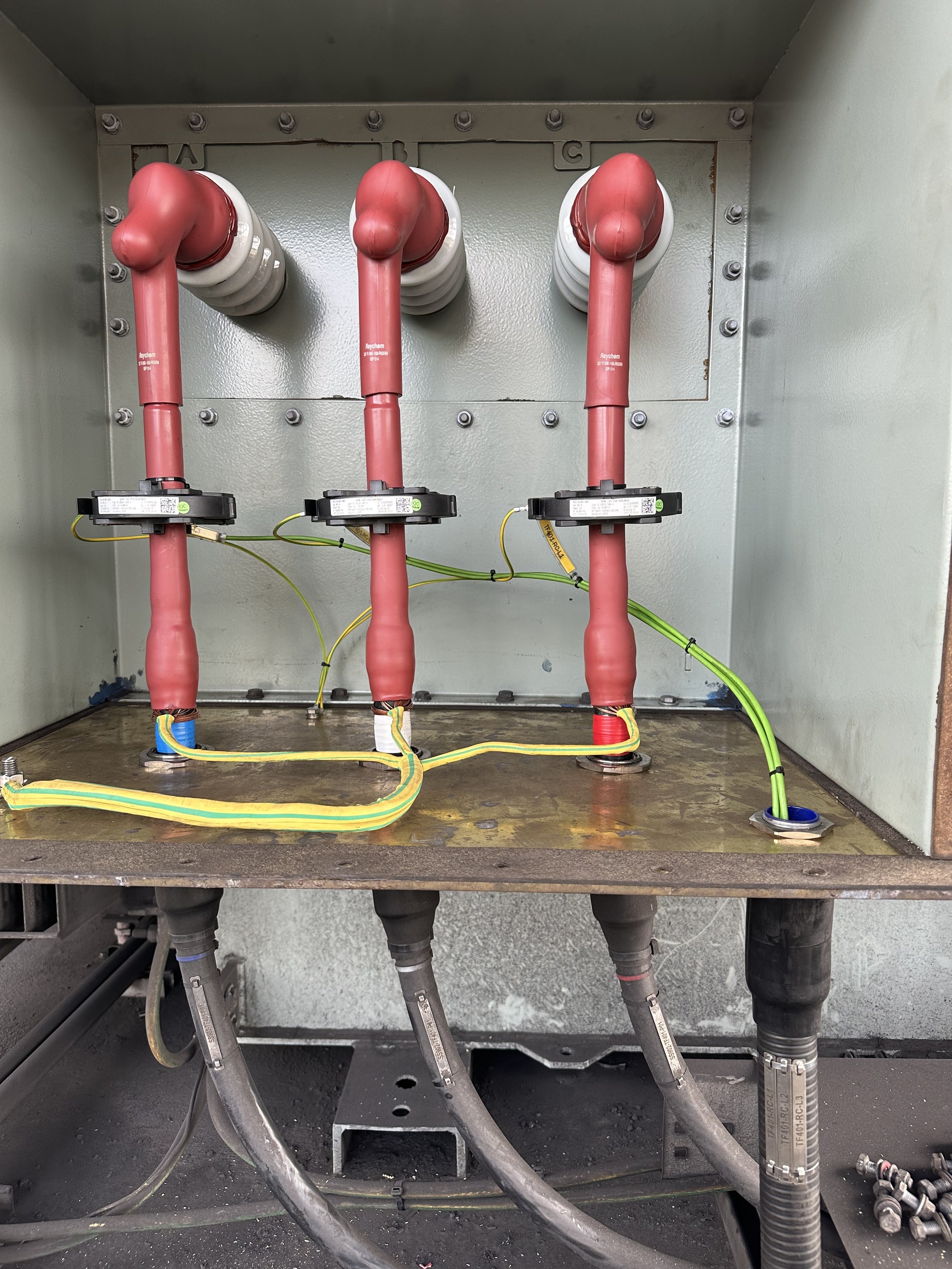 Electrical panel with three red insulated busbars and wiring connecting to circuit breakers.