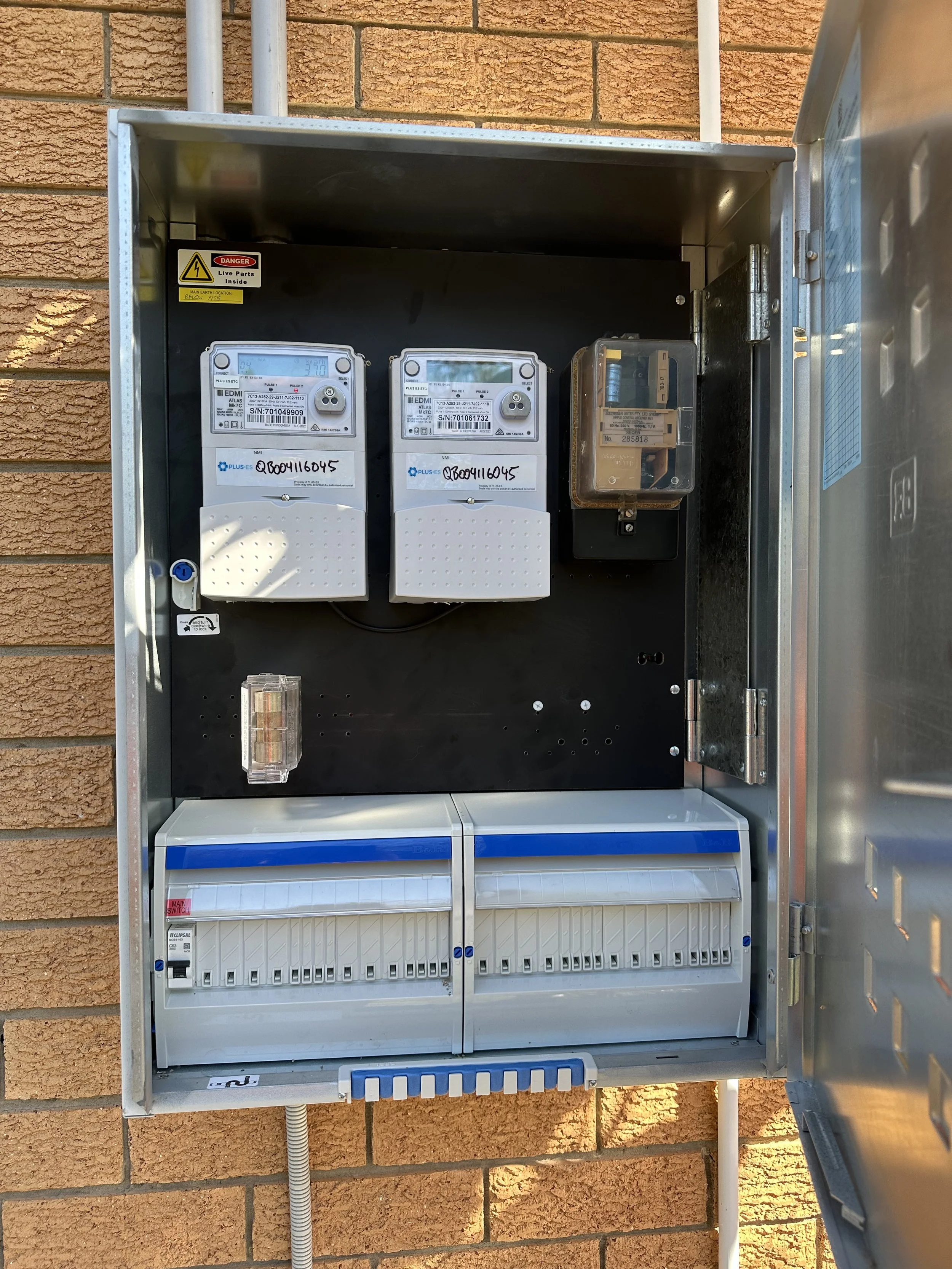 Electrical meter box mounted on a wall with brick background, open door showing meters and wiring.