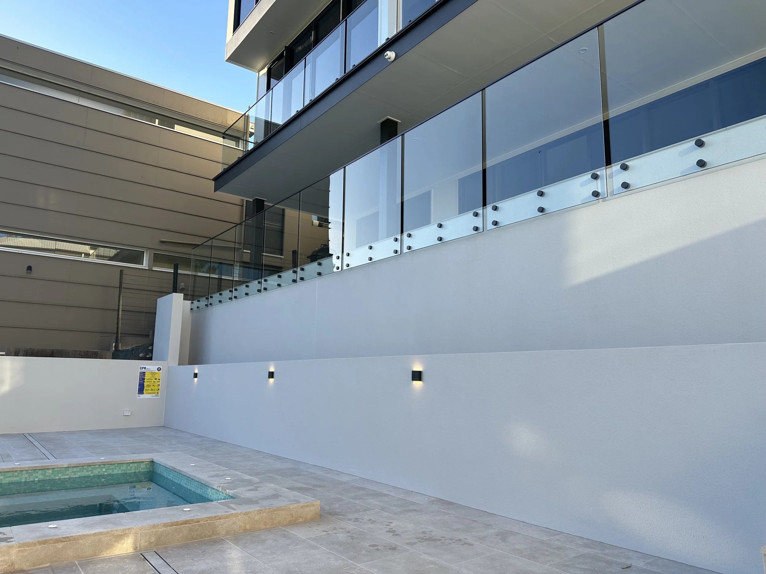 Modern building with glass balconies and beige siding, overlooking a swimming pool with tiled edge.