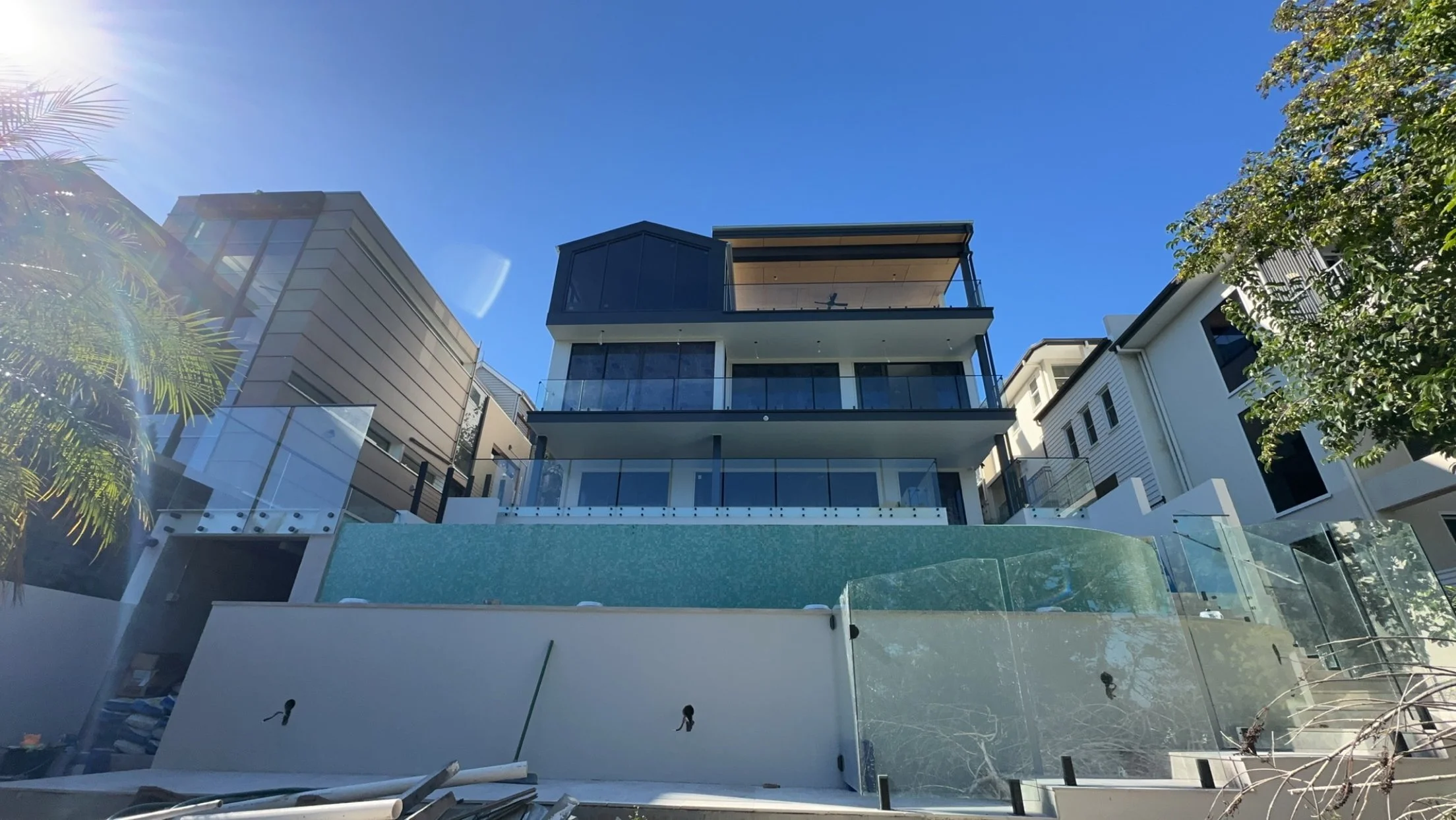 Modern multi-story house with glass balconies under a clear blue sky, seen from below.