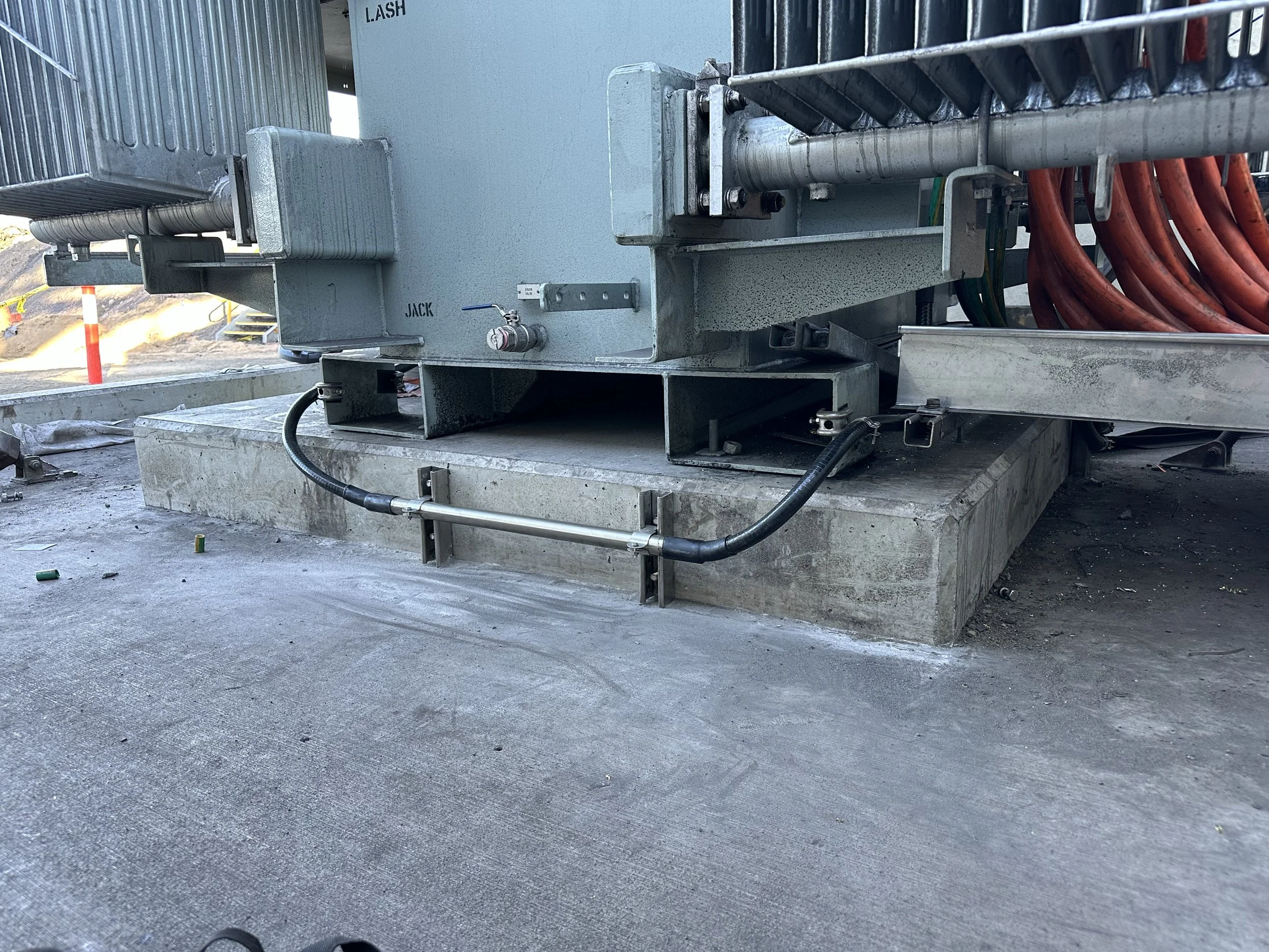 Close-up of industrial equipment and electrical wiring on a construction site, with a concrete foundation and some construction markers visible in the background.