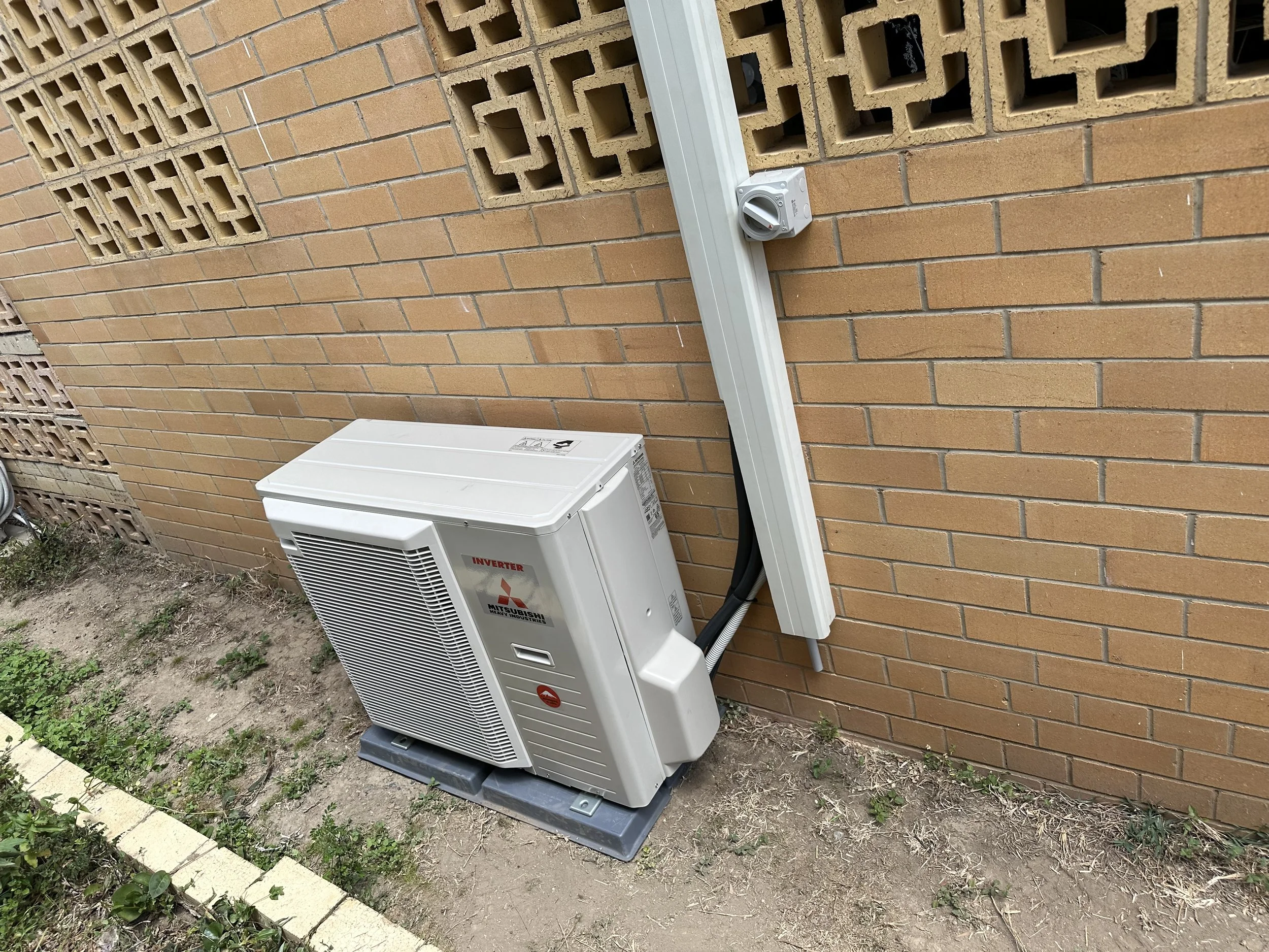 Outdoor air conditioning units attached to a brick wall with an electrical conduit and a control box.