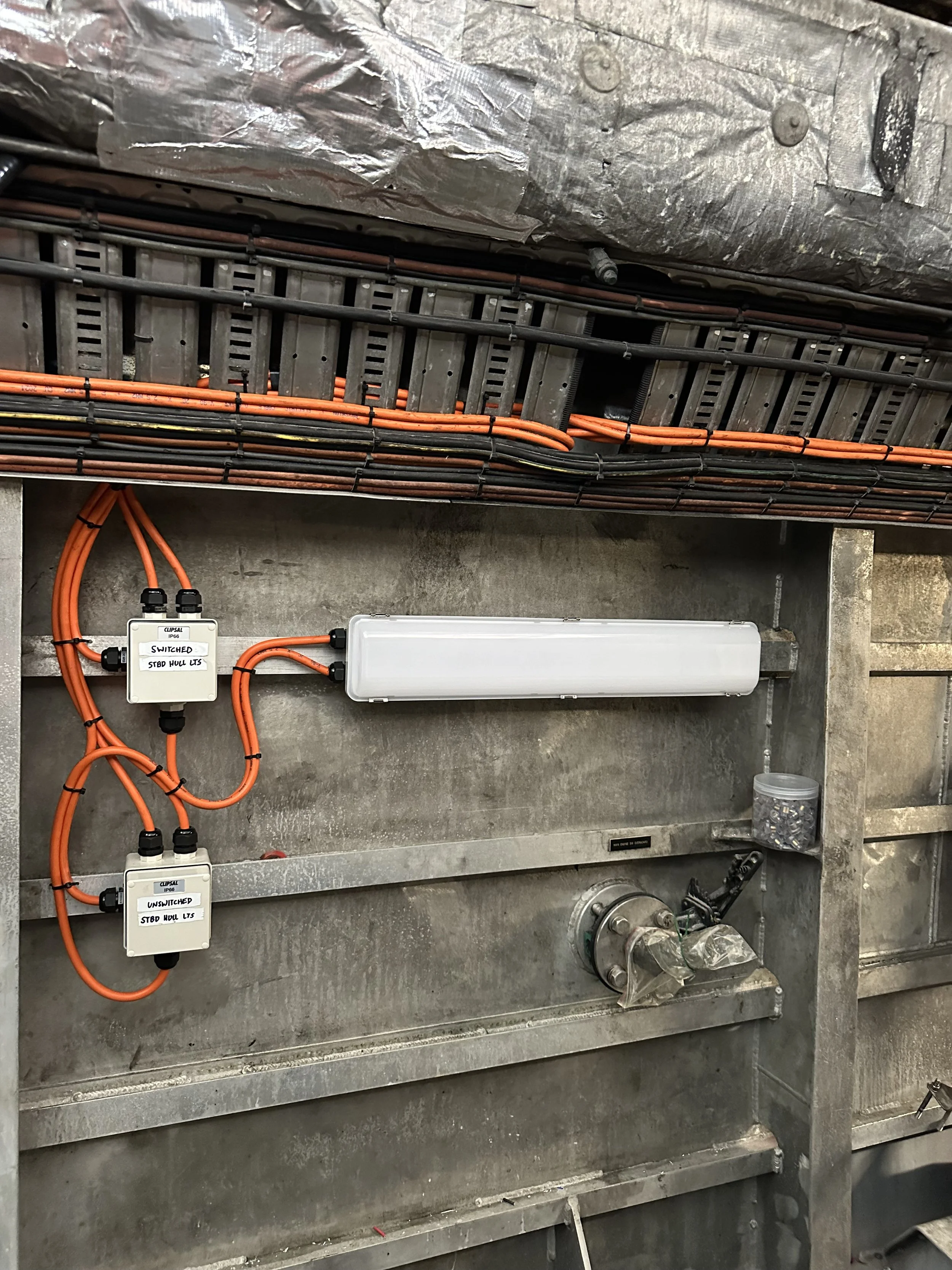 Industrial electrical panel with orange and black wires, circuit breakers, and metal components mounted inside a metallic enclosure.