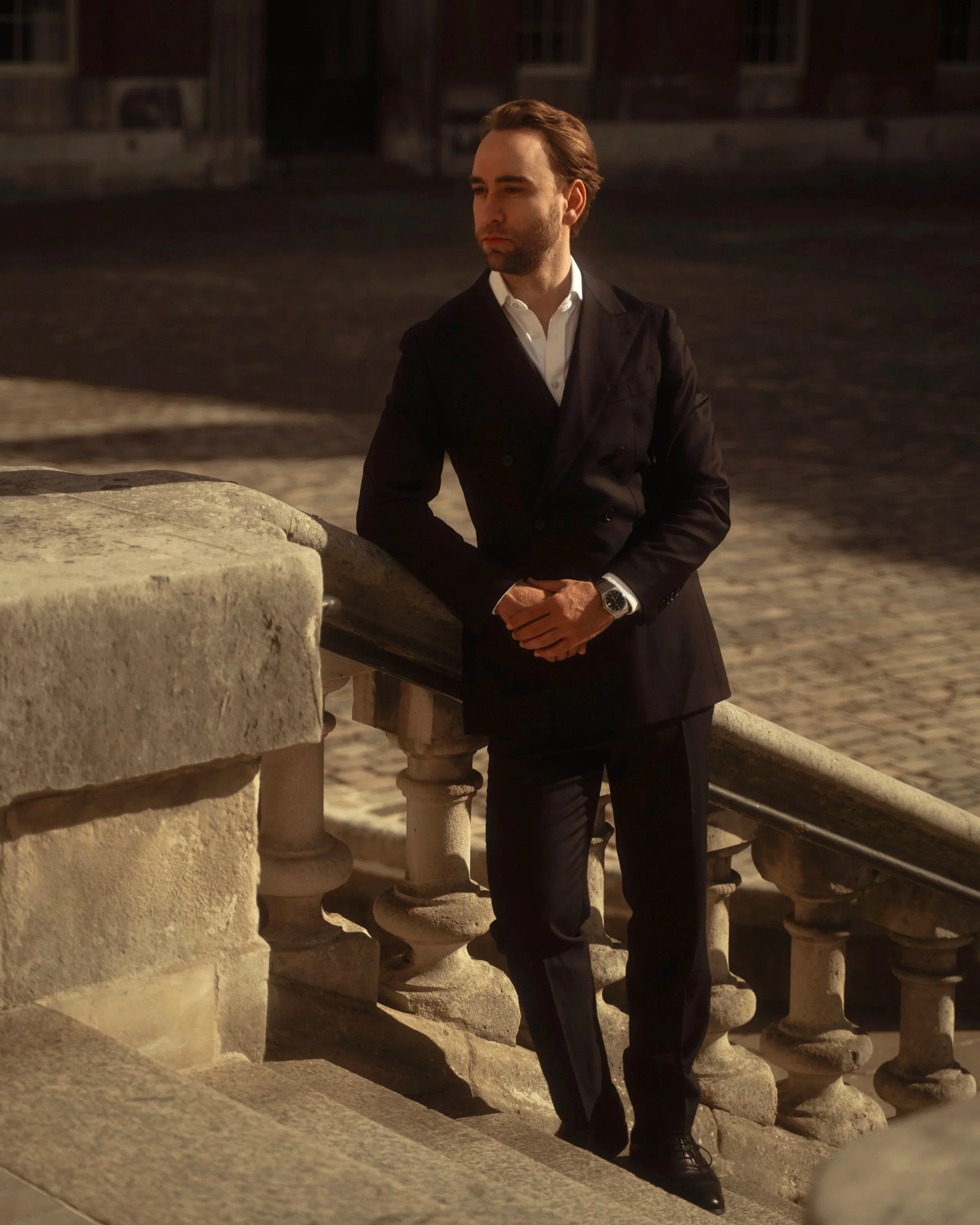 Rian Strauss, Founding Principal Partner of Strauss Partners. A man dressed in a black suit and white shirt leaning against a stone railing.