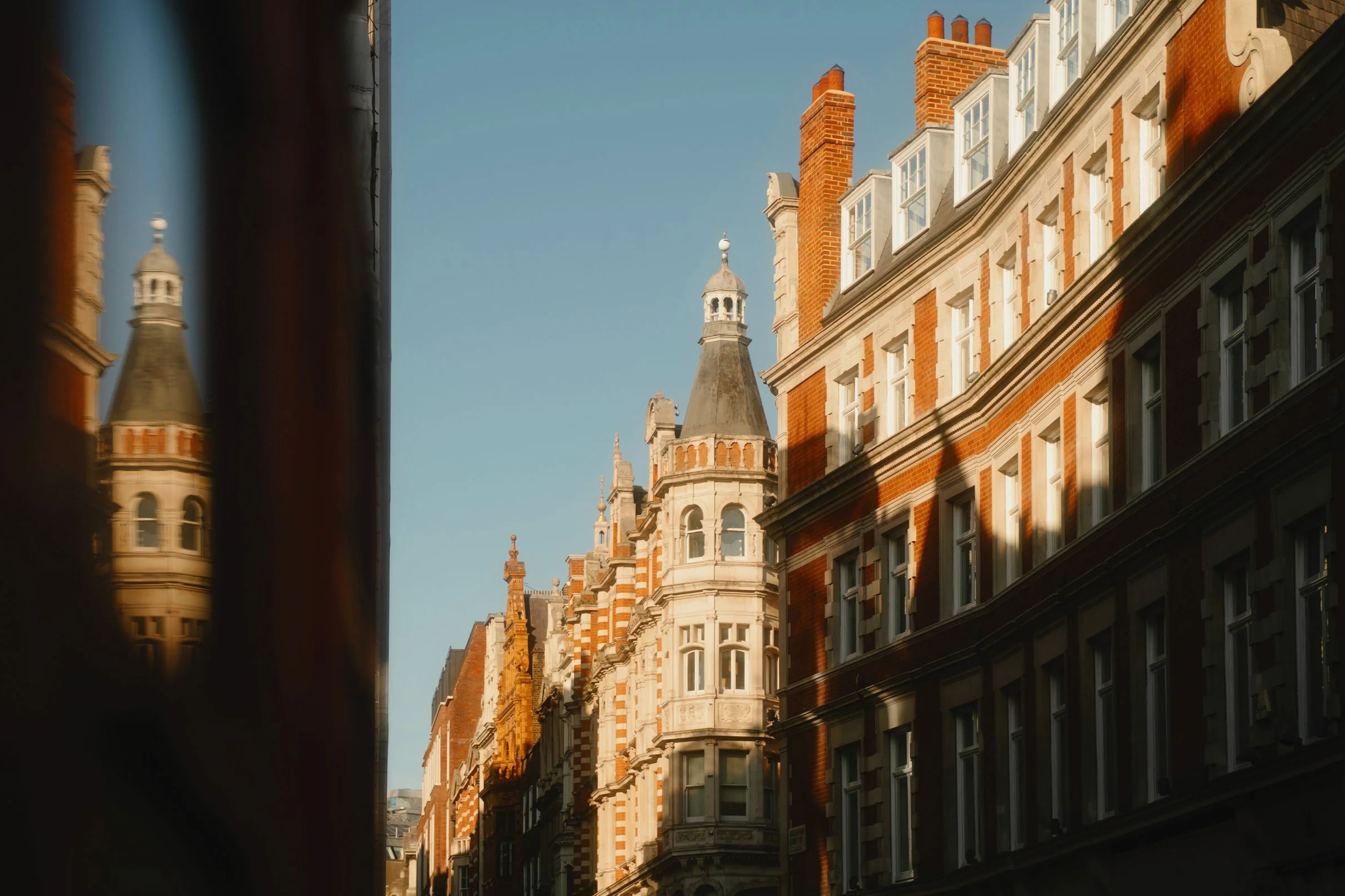 Tall, Prime London, historic brick and stone buildings with multiple chimneys, situated on a city street under a clear blue sky.