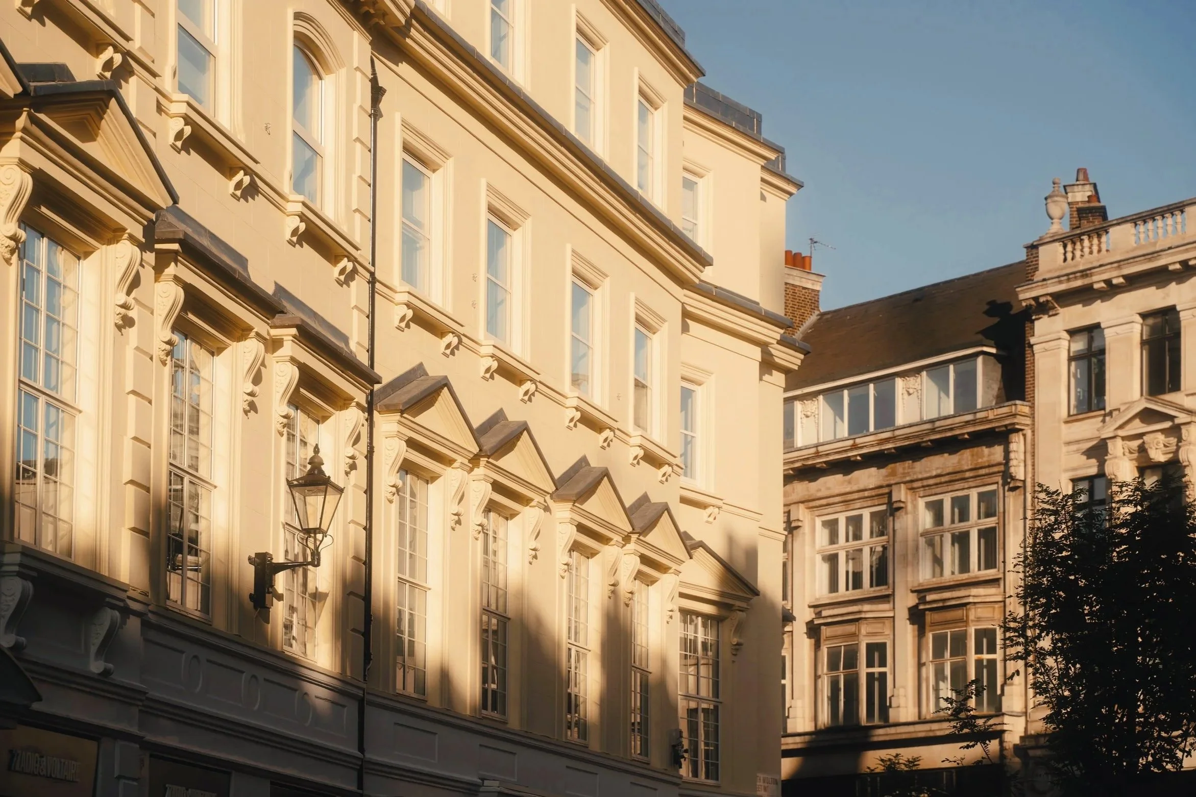 Close-up of historic beige buildings in St James, London, with detailed architectural features, large windows, and black street lamps in the foreground, under a clear evening sky.