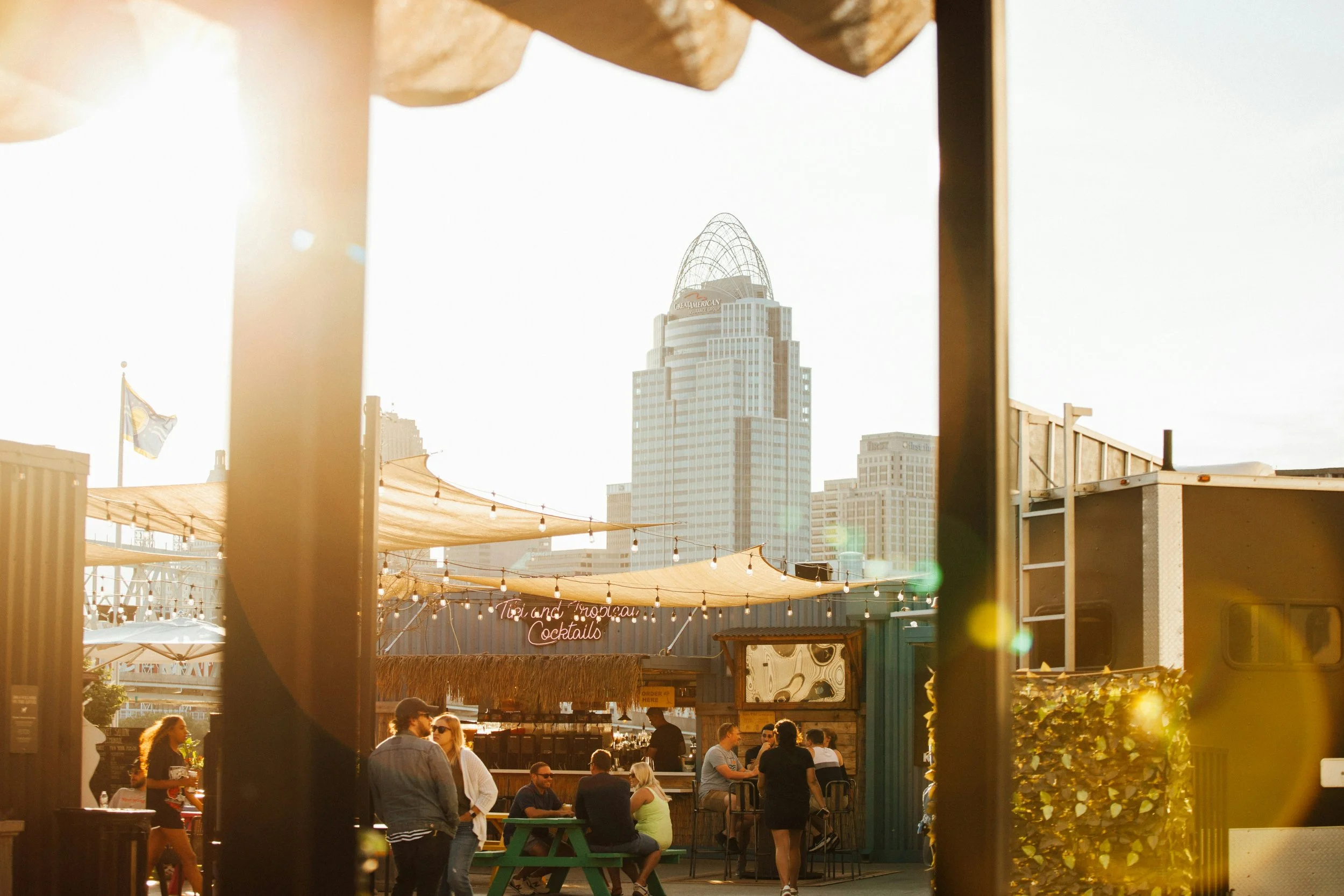 People gathered on a rooftop patio at sunset, with the Cincinnati skyline visible through wooden beams in the background