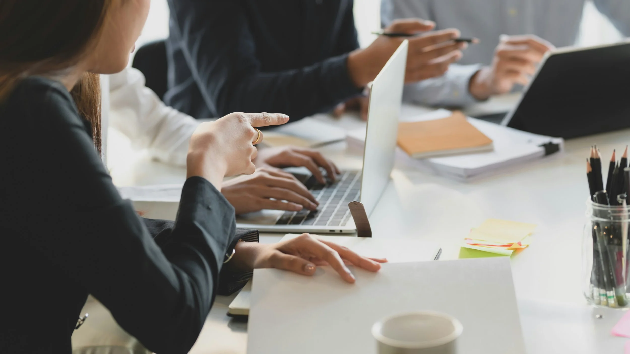 People working together at a meeting table with laptops and notebooks in an office.
