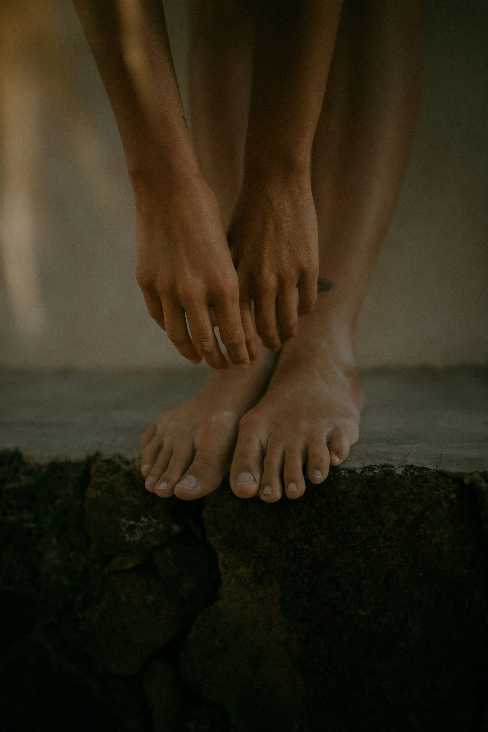 Hands and feet of a statue depicting a religious scene, with the hands holding each other's fingers and the feet standing on dark stones.