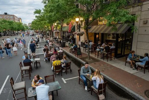 Street outdoor dining with people sitting at tables outside a restaurant.