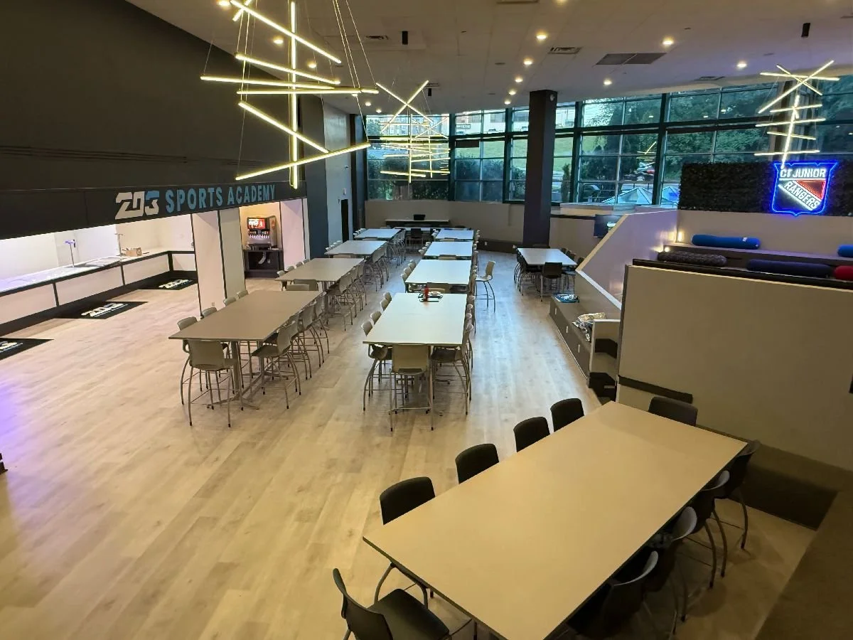 Empty sports bar or recreational lounge with multiple tables, chairs, large windows, modern lighting, and sports-themed decor.