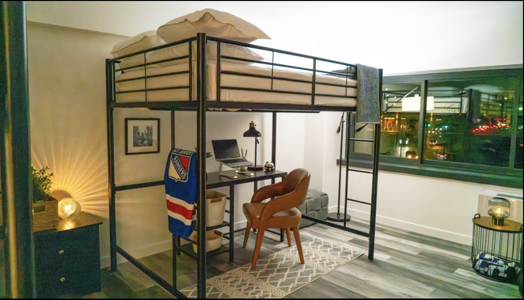 Loft bed with a workspace underneath, including a computer and a leather chair, in a modern apartment.