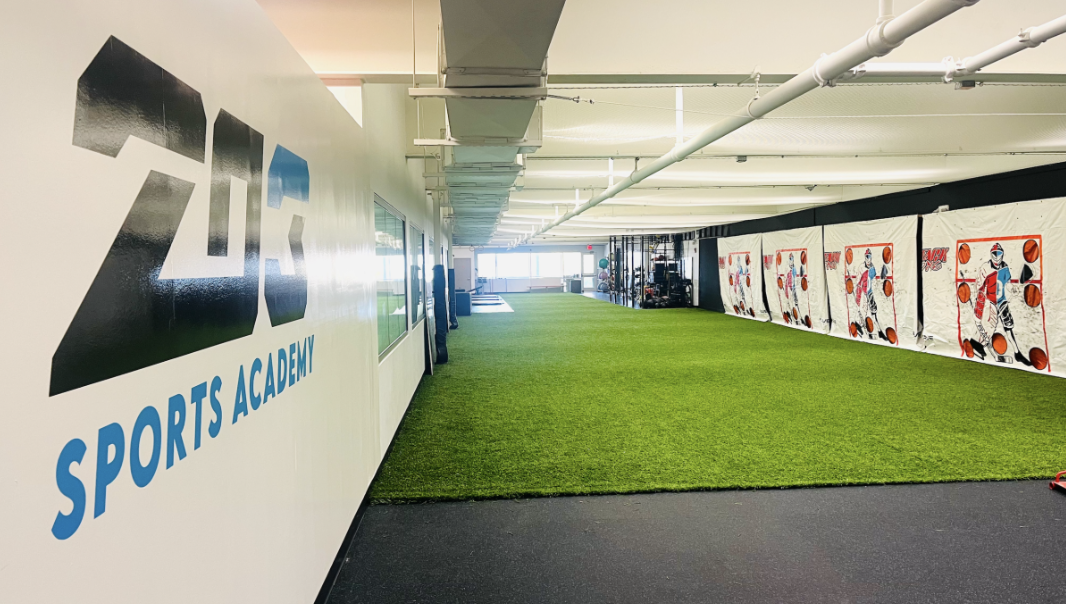 Indoor sports training facility with artificial turf, sports equipment, and a wall with cartoon athlete posters at ZO Sports Academy.